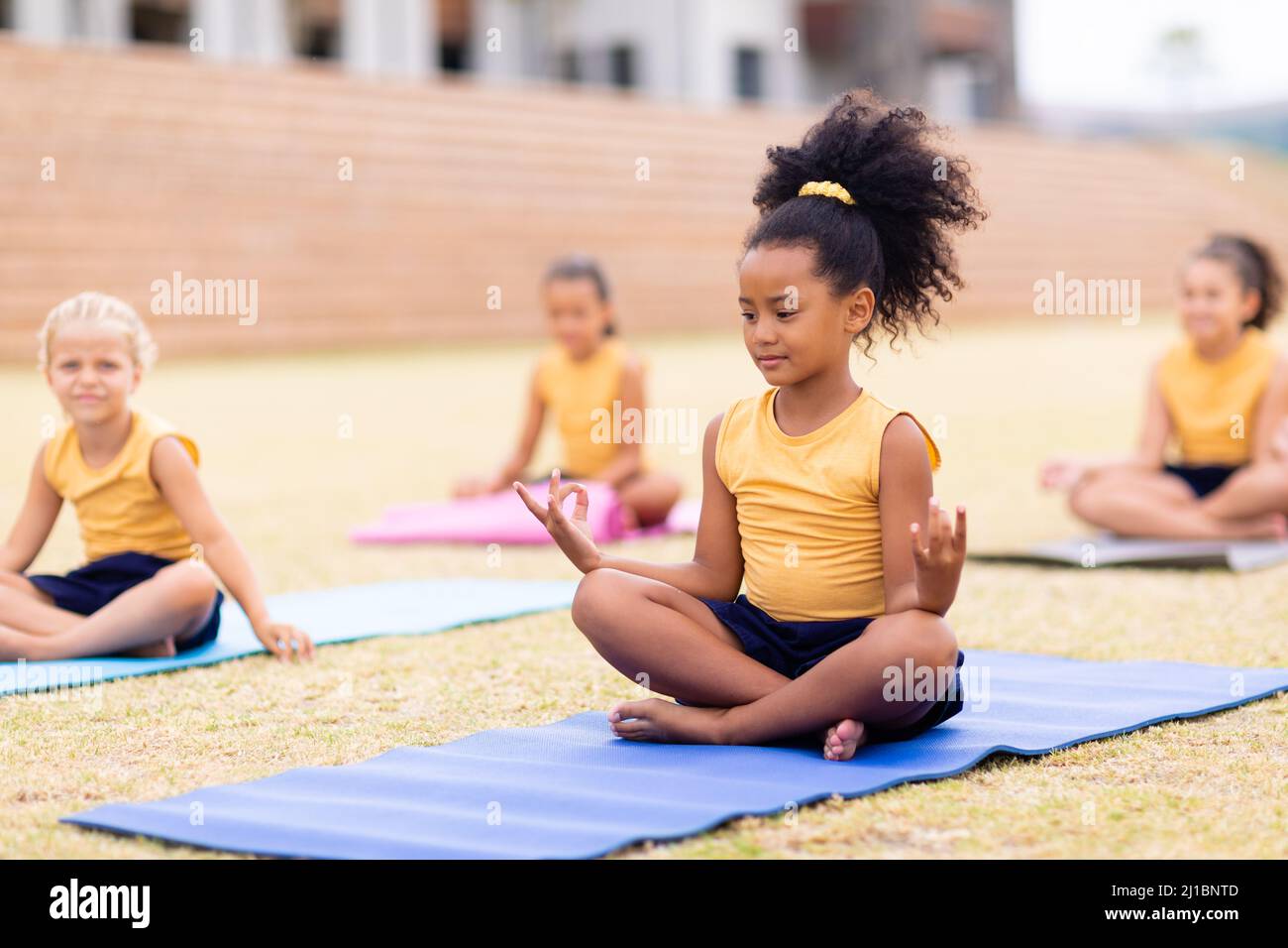 Multirassische Grundschüler mit Gestik, während sie auf der Yogamatte auf dem Schulgelände sitzen Stockfoto