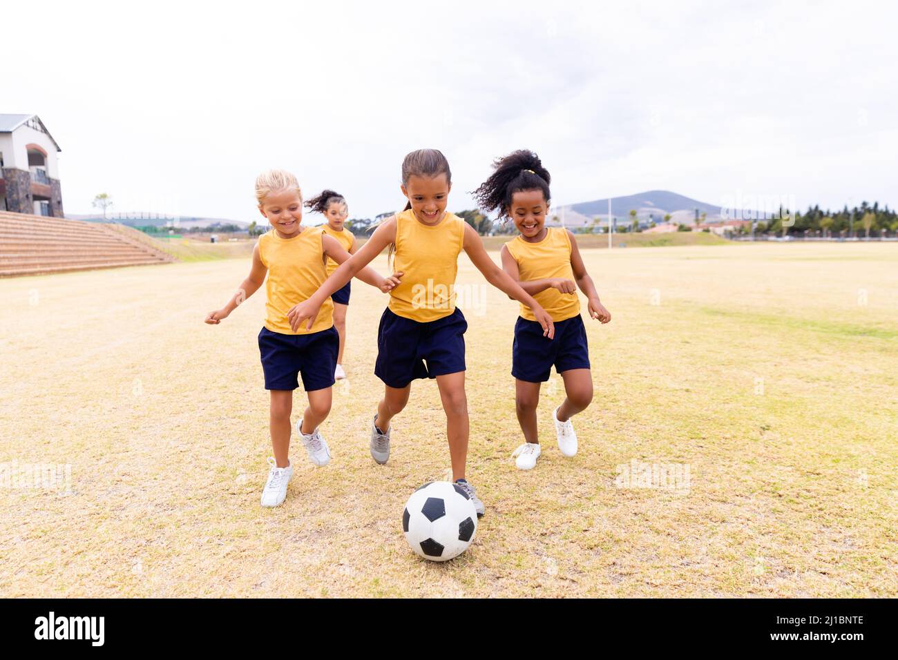 Die ganze Länge der multirassischen Grundschüler, die auf dem Schulgelände Fußball spielen Stockfoto
