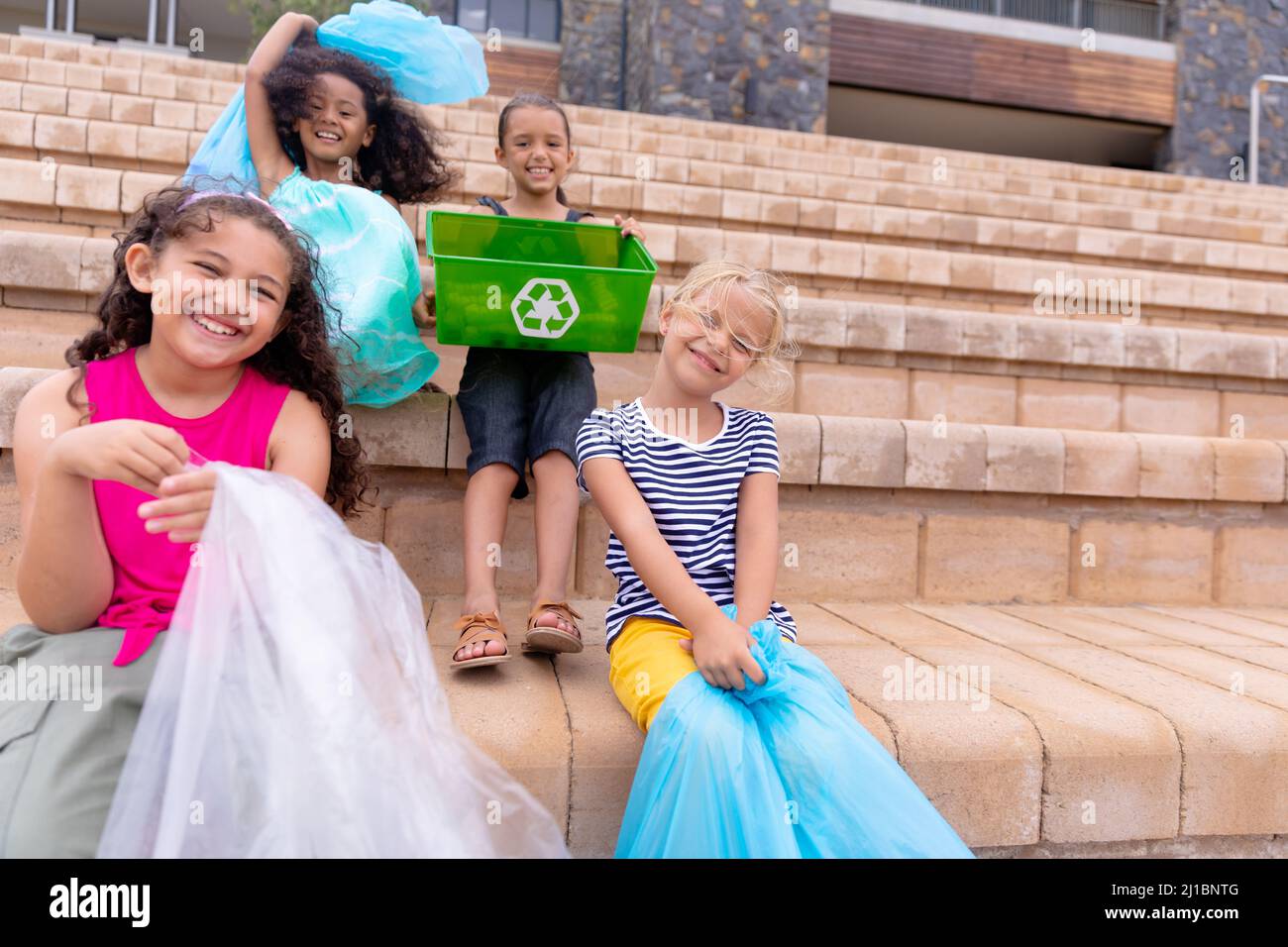 Portrait fröhliche multirassische Grundschüler mit Mülltüten auf der Schultreppe Stockfoto