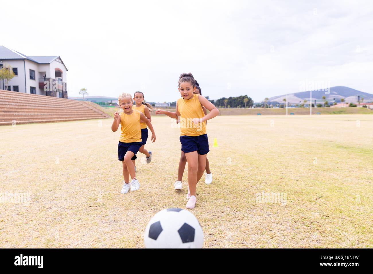 Multirassische Grundschüler, die auf den Fußball zulaufen, während sie auf dem Boden Fußball spielen Stockfoto