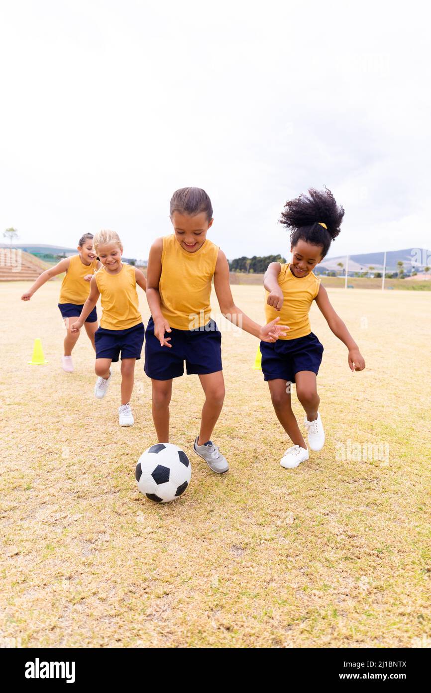 In voller Länge fröhliche multirassische Grundschüler, die auf dem Schulgelände Fußball spielen Stockfoto