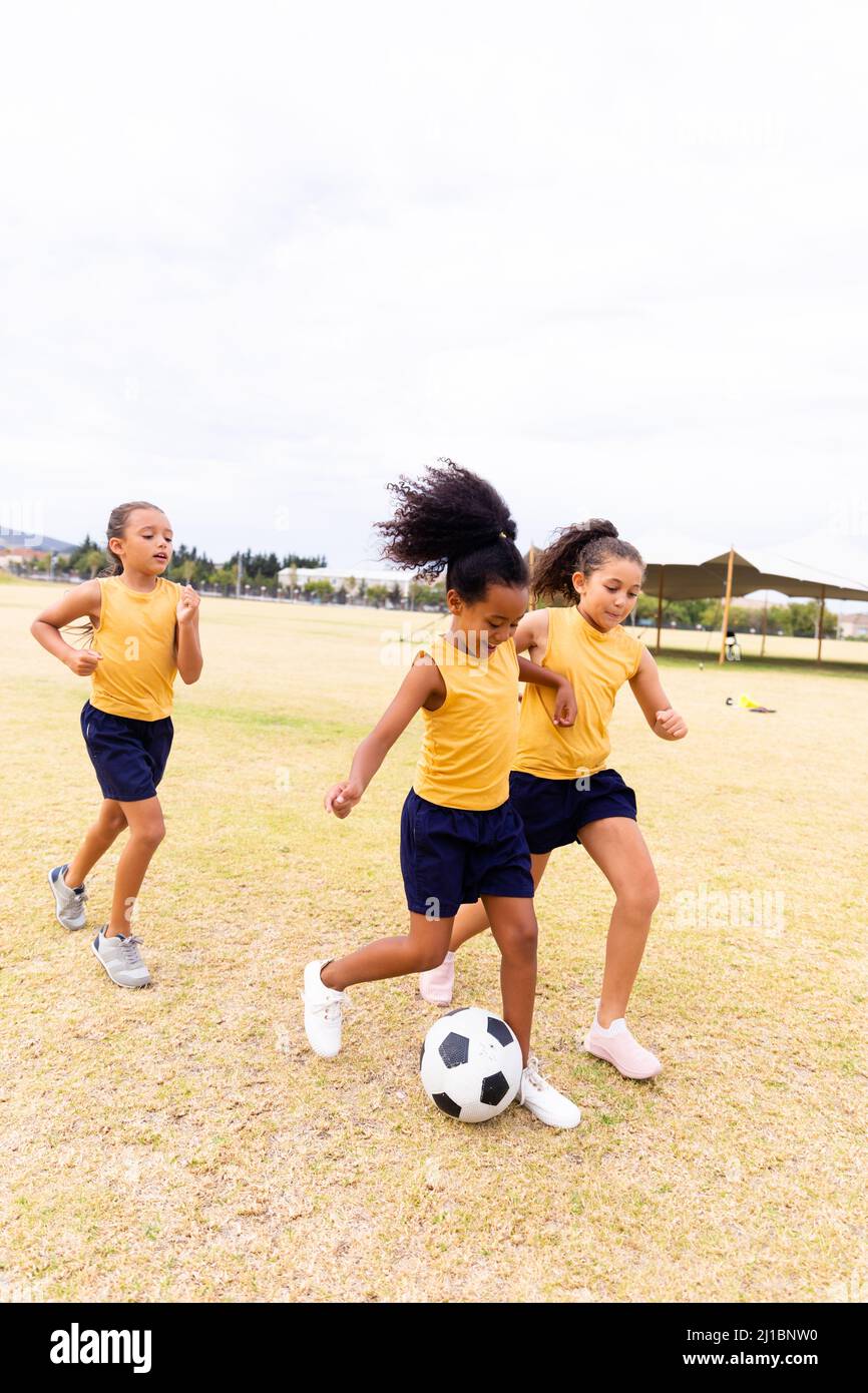 Die ganze Länge der multirassischen Grundschüler, die auf dem Schulgelände gegen den Himmel Fußball spielen Stockfoto
