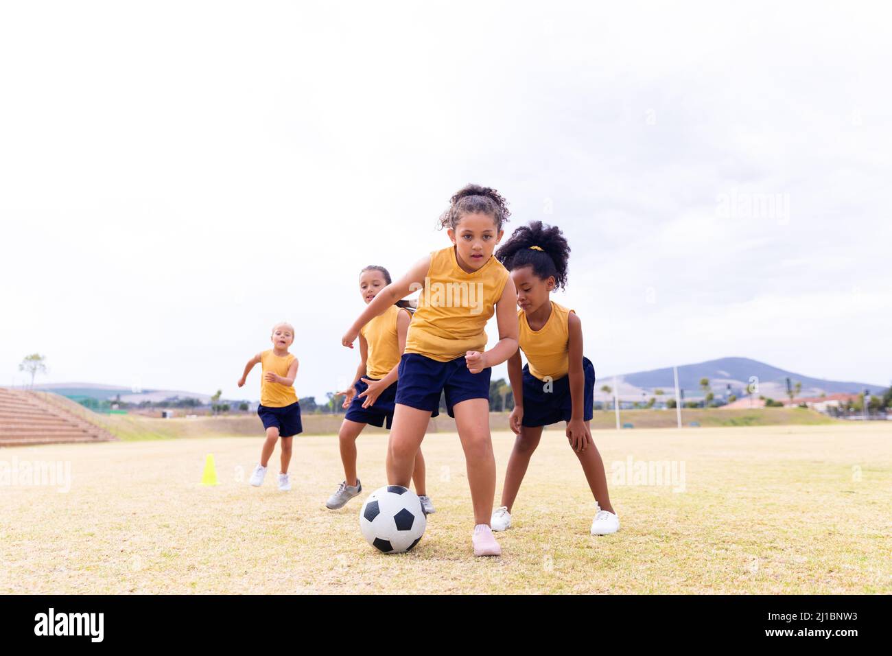In voller Länge multirassische Grundschüler in Sportuniform Fußball gegen Himmel spielen Stockfoto