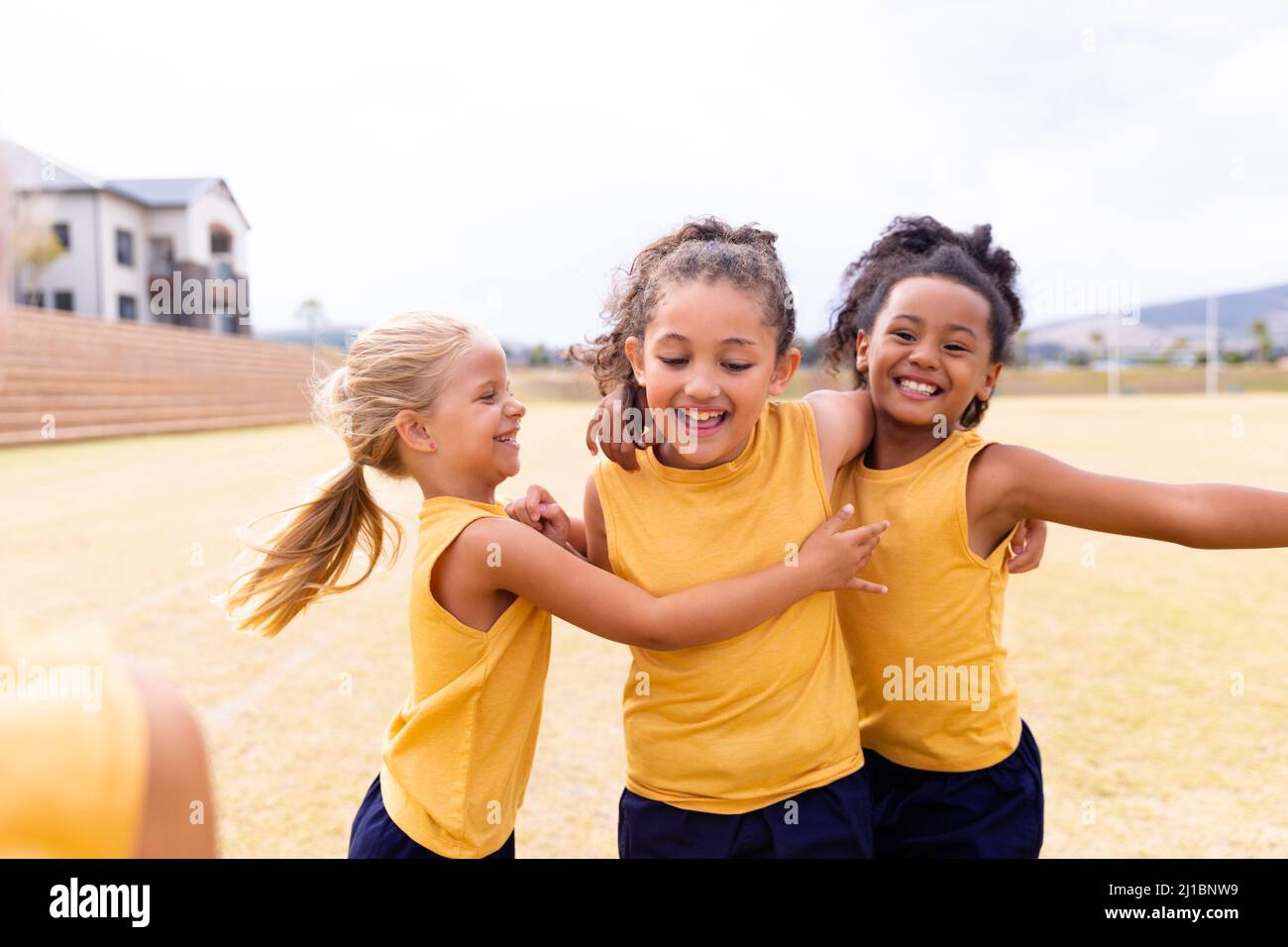 Fröhliche multirassische Grundschüler in Sportuniform auf dem Boden während des Fußballsports Stockfoto