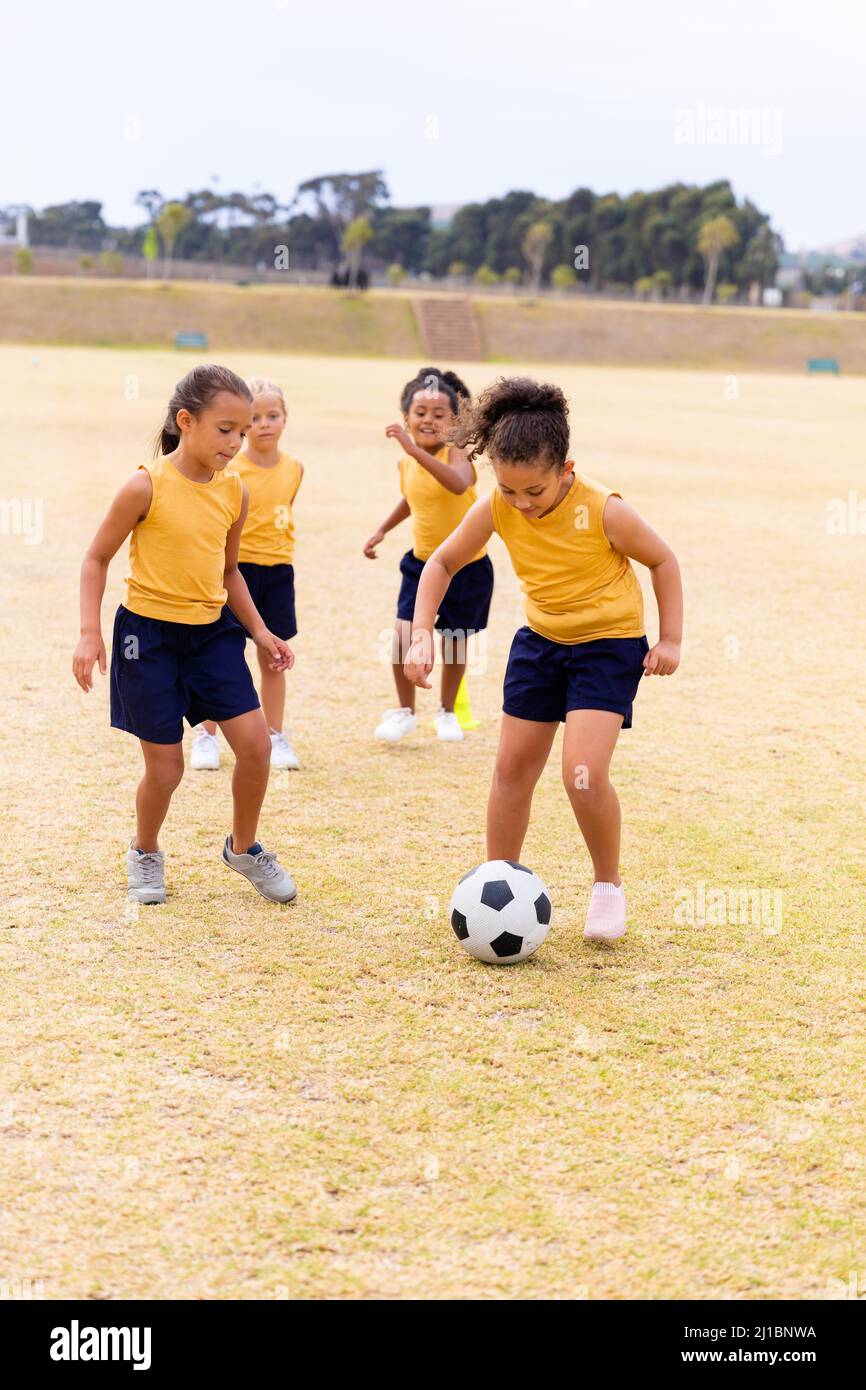 Die gesamte Länge der multirassischen Grundschüler läuft beim Fußballspielen auf dem Schulgelände Stockfoto