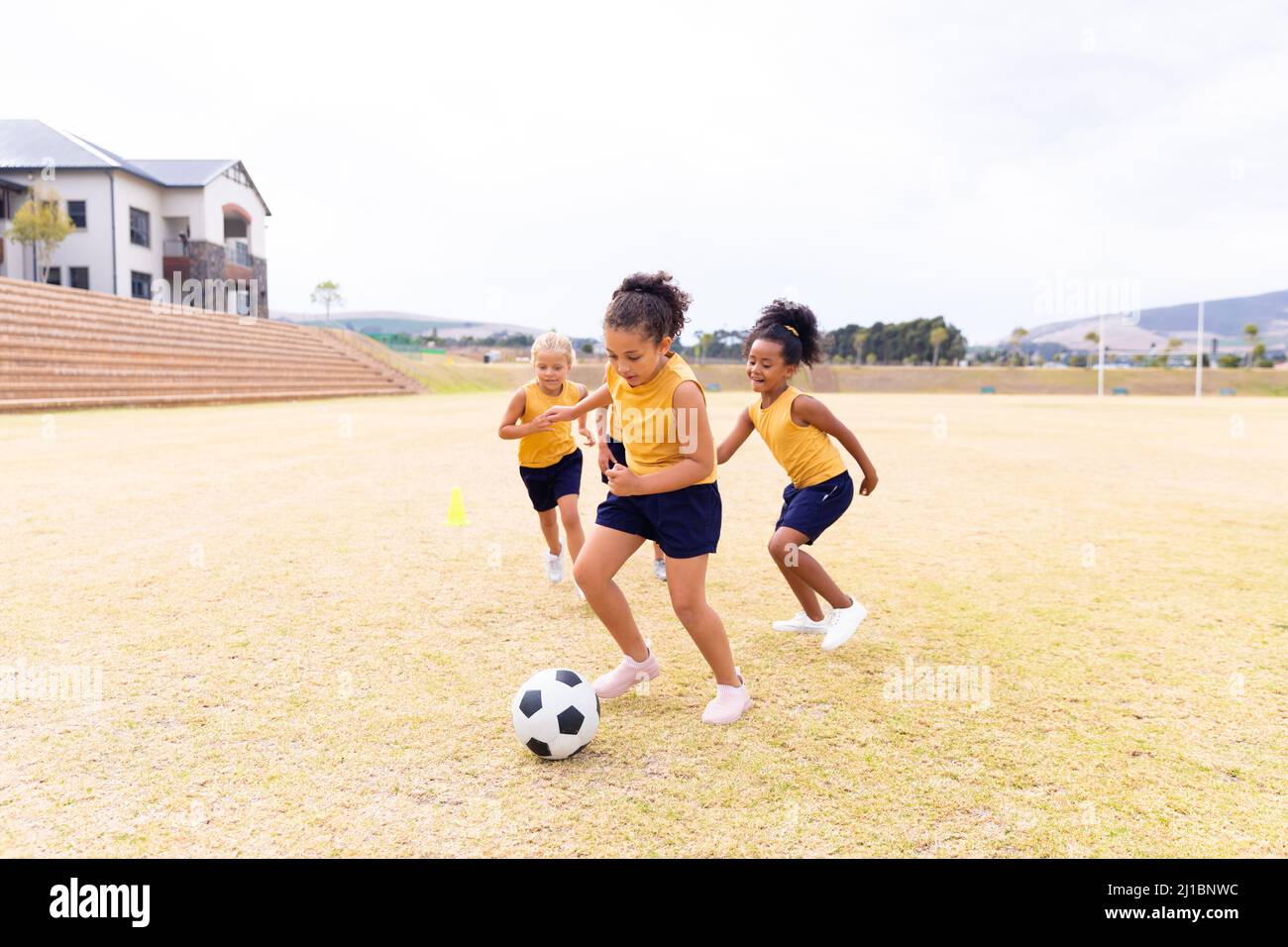 Multirassische Grundschüler in Sportuniform, die auf dem Schulgelände gegen den Himmel Fußball spielen Stockfoto
