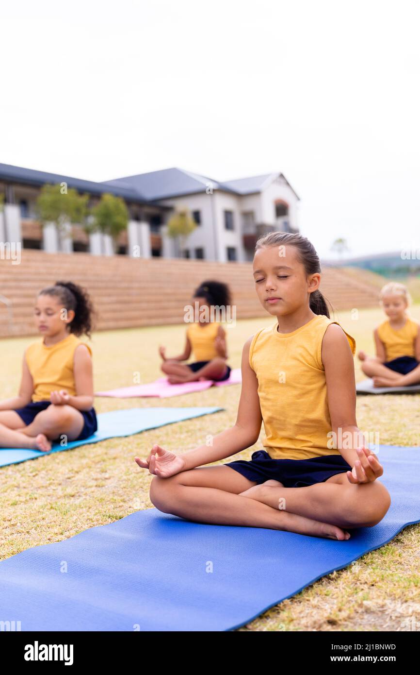 Multirassische Grundschüler meditieren, während sie auf dem Schulgelände auf einer Übungsmatte sitzen Stockfoto