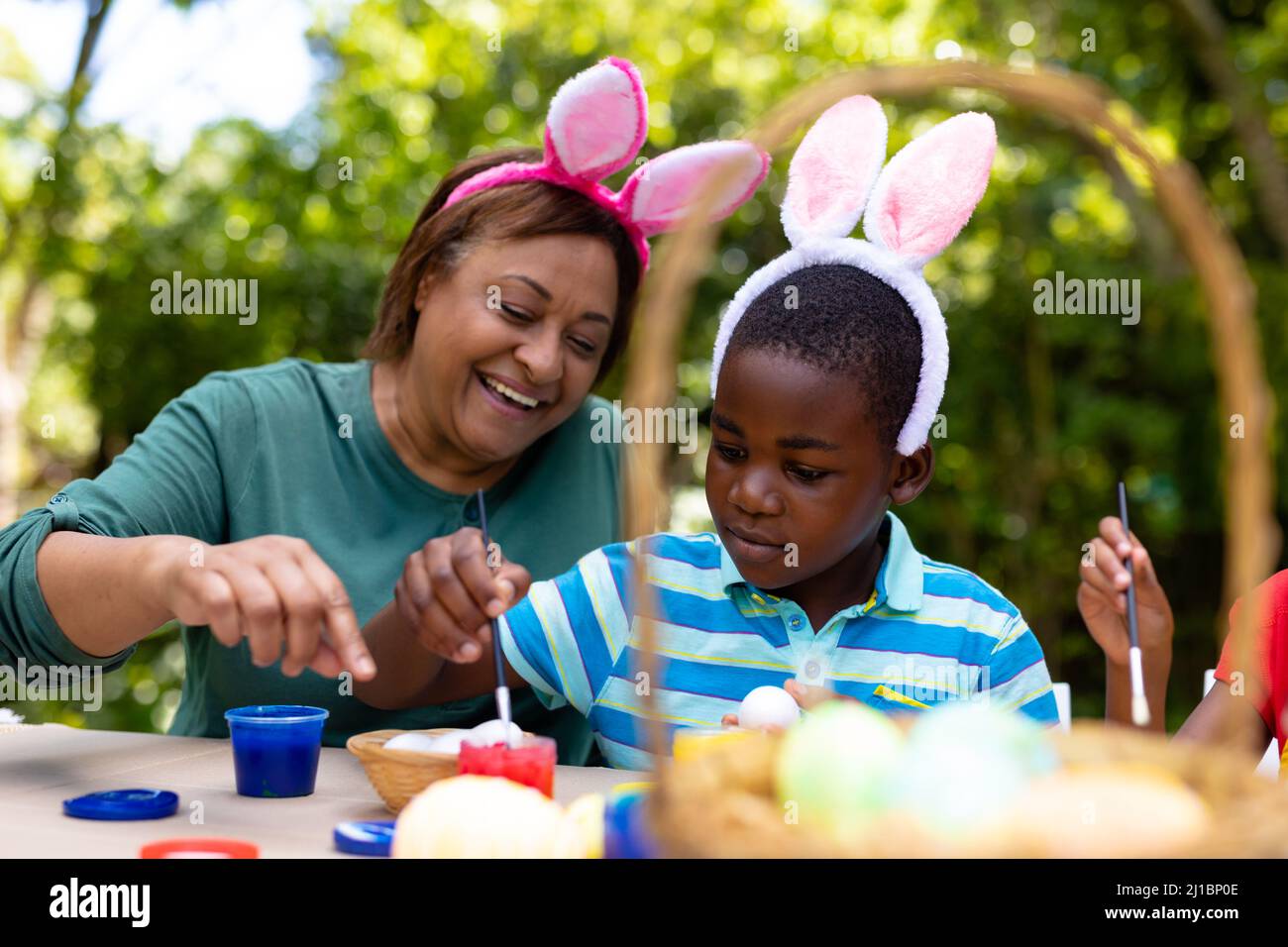 afroamerikanischer Junge und Großmutter tragen Hasenohren, während sie am ostertag Eier malen Stockfoto