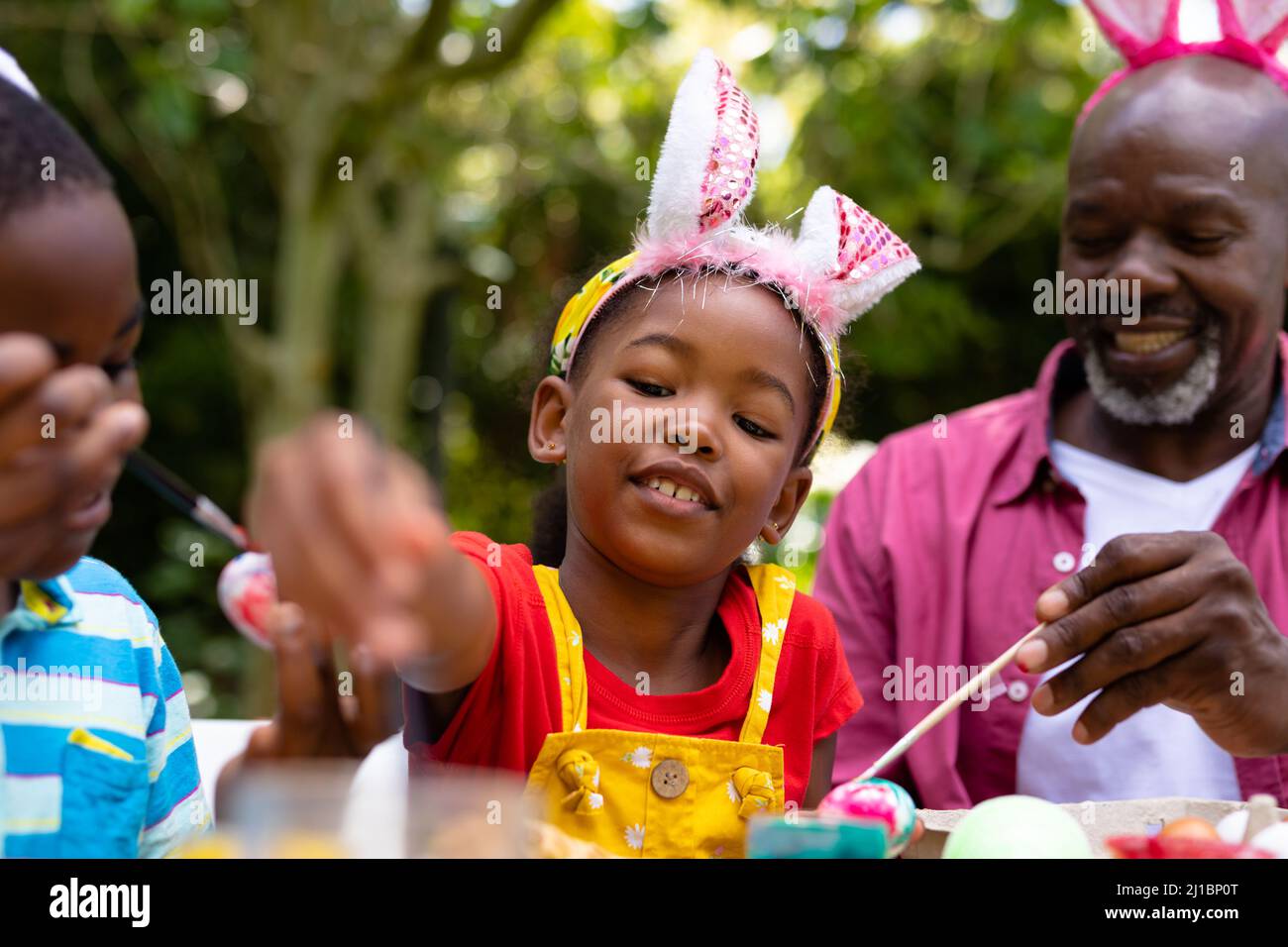 afroamerikanische Geschwister und Großvater in Hasenohren malen am ostertag Eier Stockfoto
