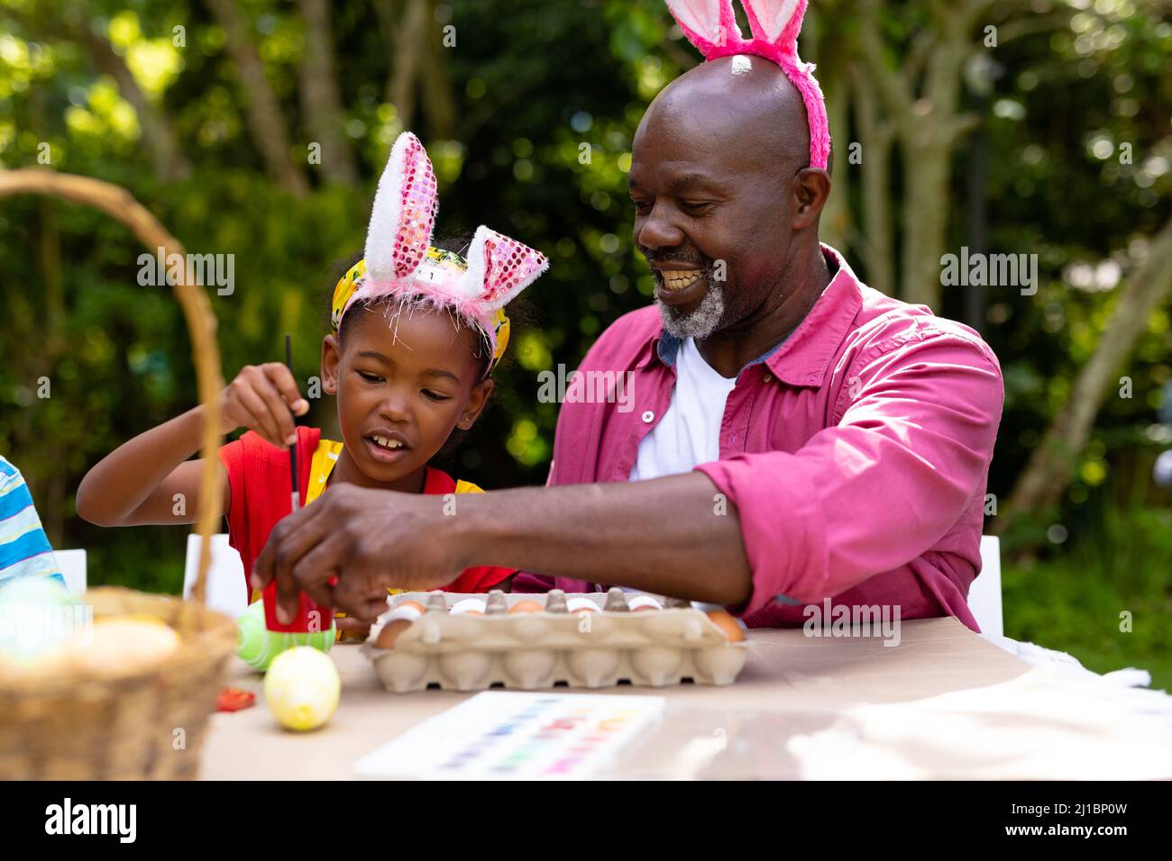 afroamerikanisches Mädchen und Großvater tragen Hasenohren, während sie am ostertag Eier malen Stockfoto