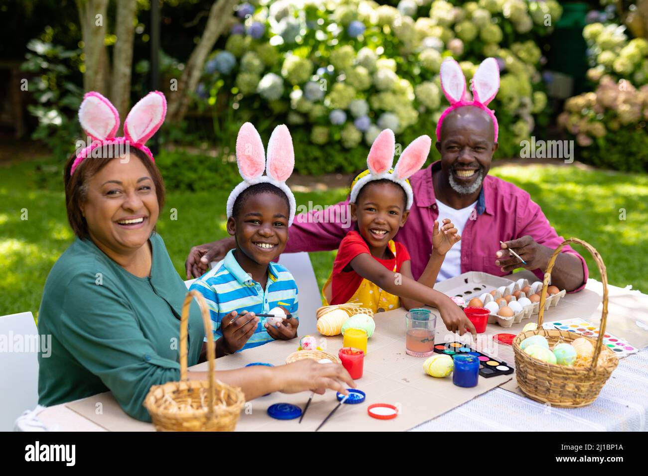 Porträt glücklicher afroamerikanischer Geschwister und Großeltern in Hasenohren, die Ostereier malen Stockfoto