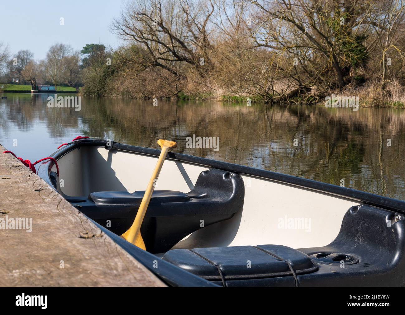 Ein Kanu mit Paddel wird an einem sonnigen Tag an einer Landebahn auf einem Fluss festgebunden Stockfoto