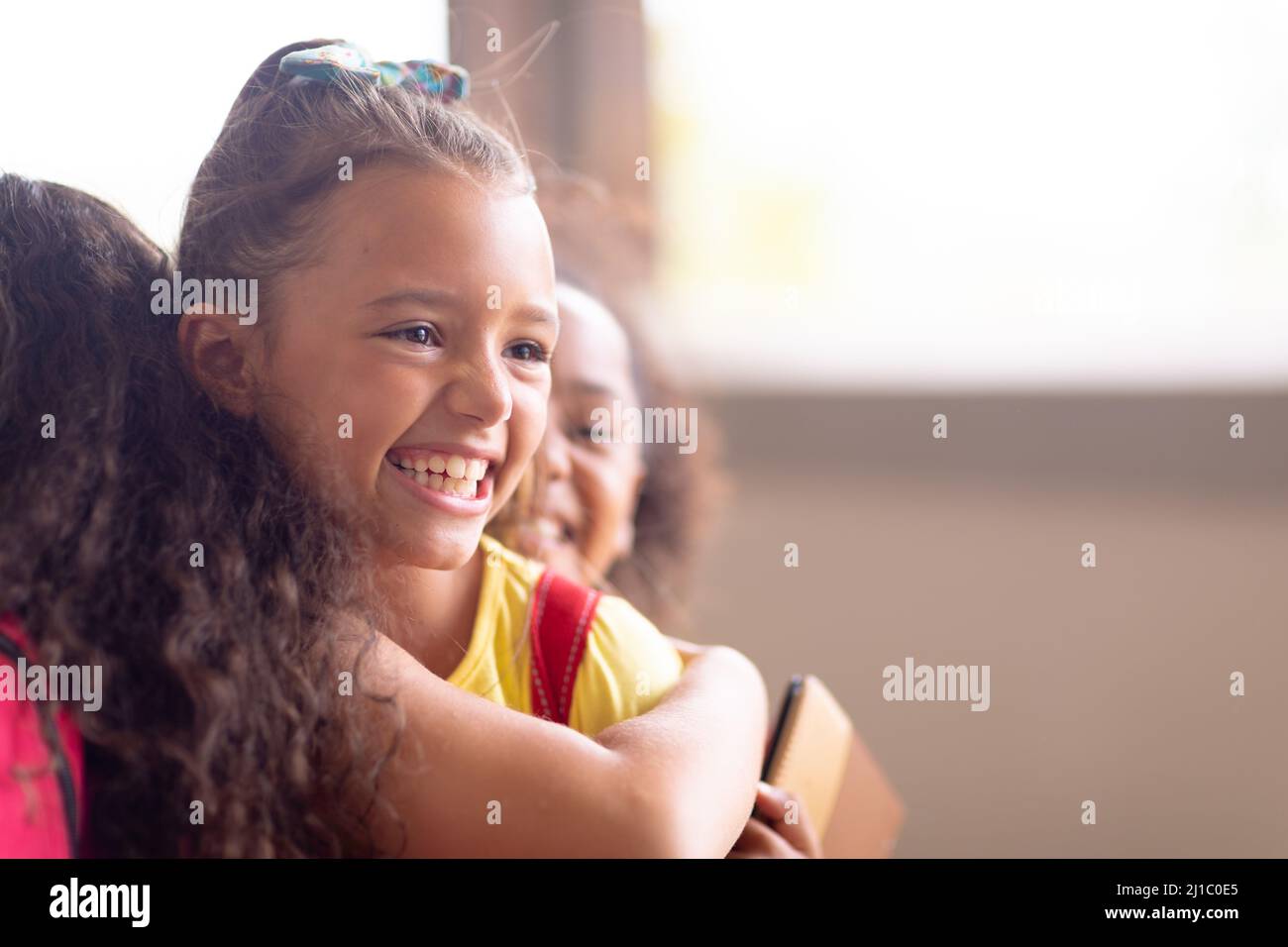 Nahaufnahme von multirassischen, fröhlichen Grundschulmädchen, die sich während des Stehens in der Schule umarmen Stockfoto