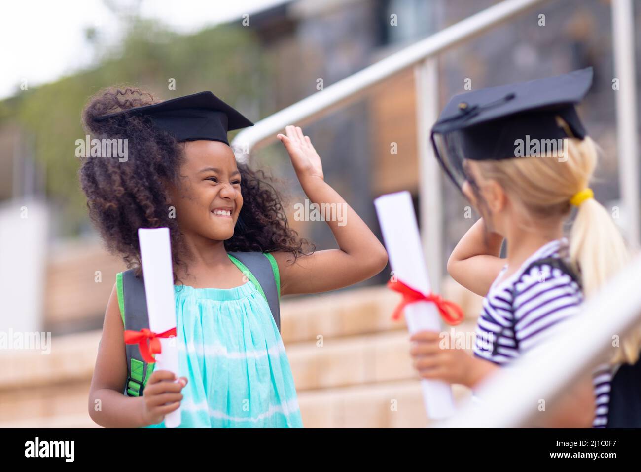 Fröhliche multirassische Grundschüler mit Leichenbrettern und einem hohen Grad auf Stufen Stockfoto