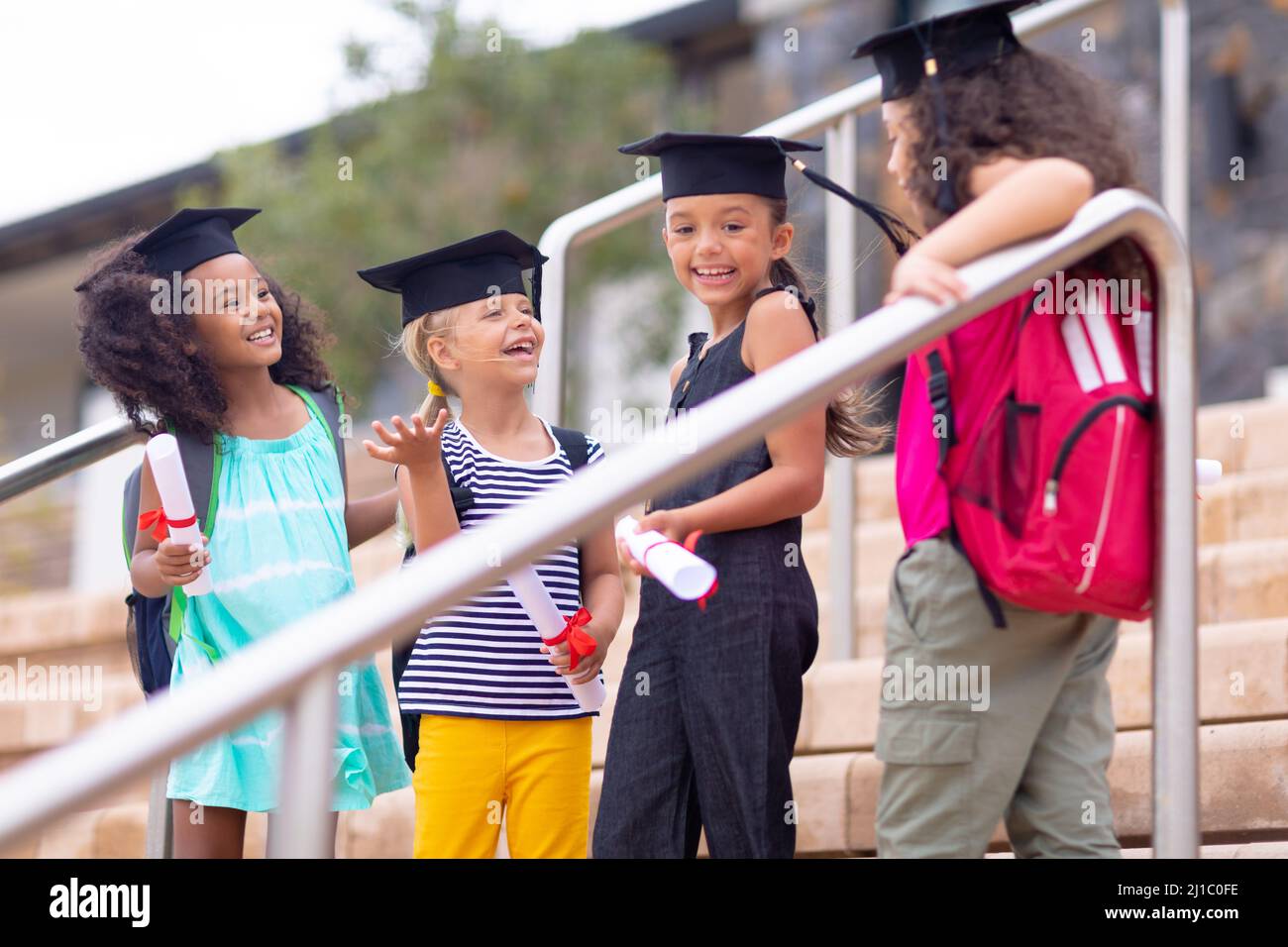 Fröhliche multirassische Grundschüler mit Grad und Leichenbrettern, die auf Stufen stehen Stockfoto