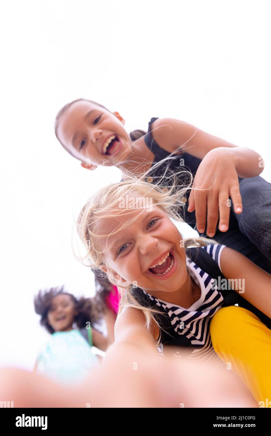 Porträt eines verspielten multirassischen Grundschulmädchen, das gegen den Himmel steht Stockfoto