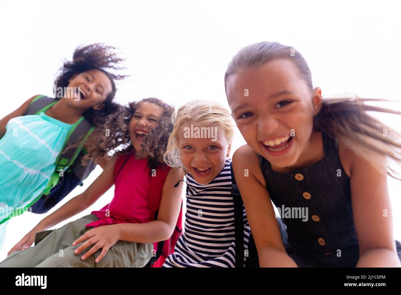 Porträt von fröhlichen, multirassischen Grundschülerinnen, die gegen den Himmel stehen Stockfoto