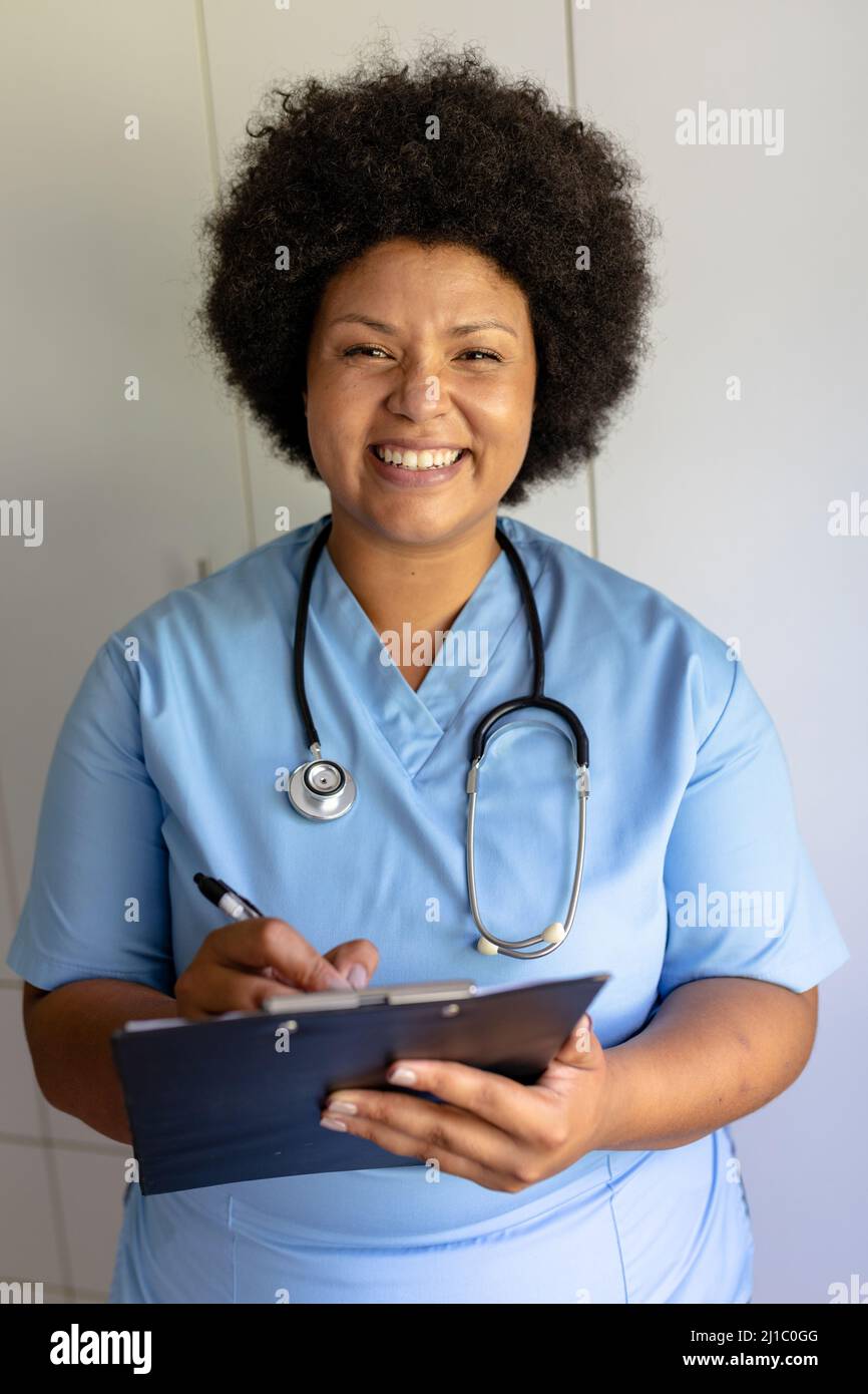 Porträt einer lächelnden afroamerikanischen Krankenschwester mit mittlerem Erwachsenen, die im Krankenhaus auf die Zwischenablage schreibt Stockfoto