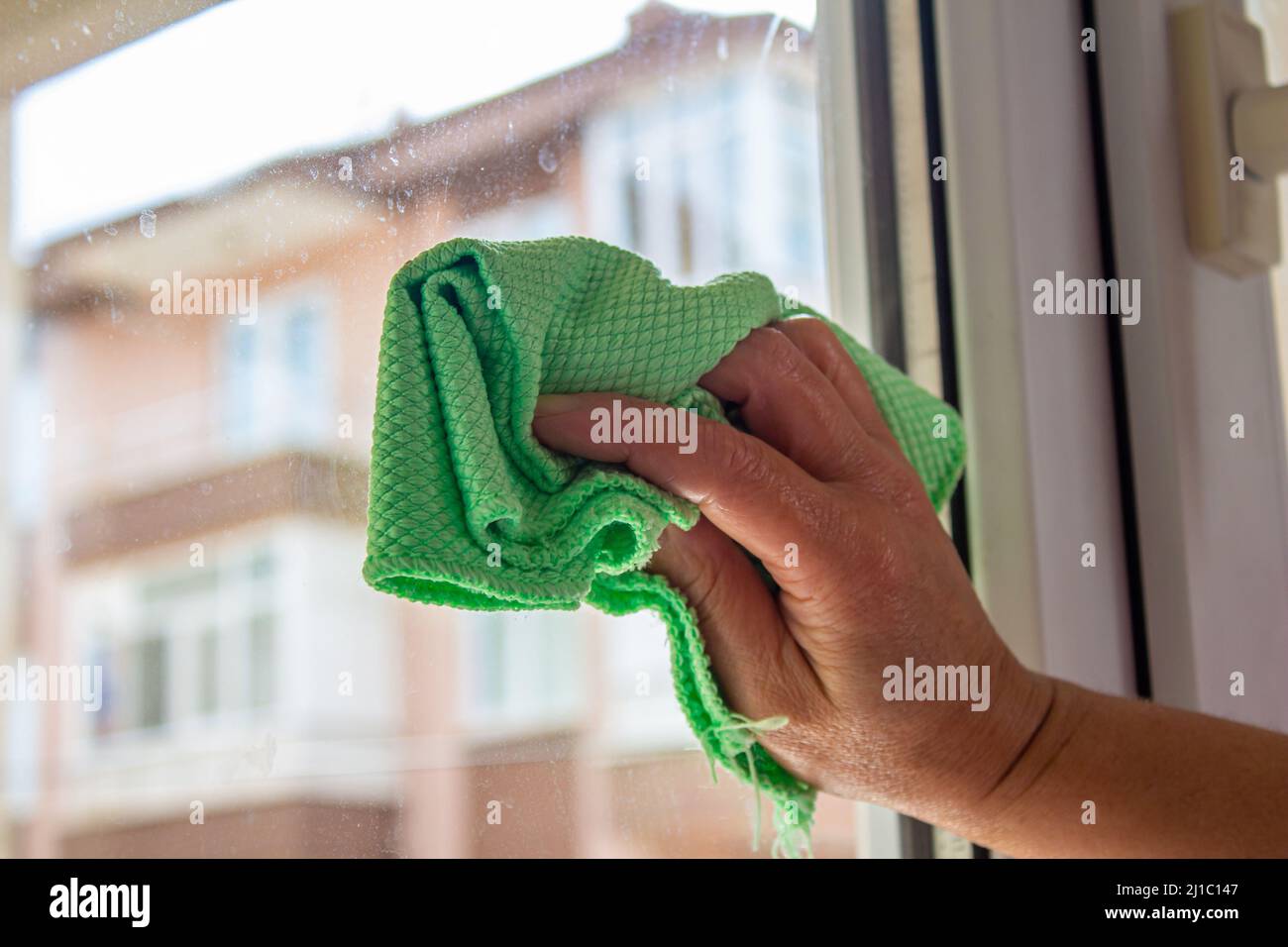 Fenster mit grünem Tuch reinigen. Hausarbeit. Frau macht die Haushaltung. Stockfoto