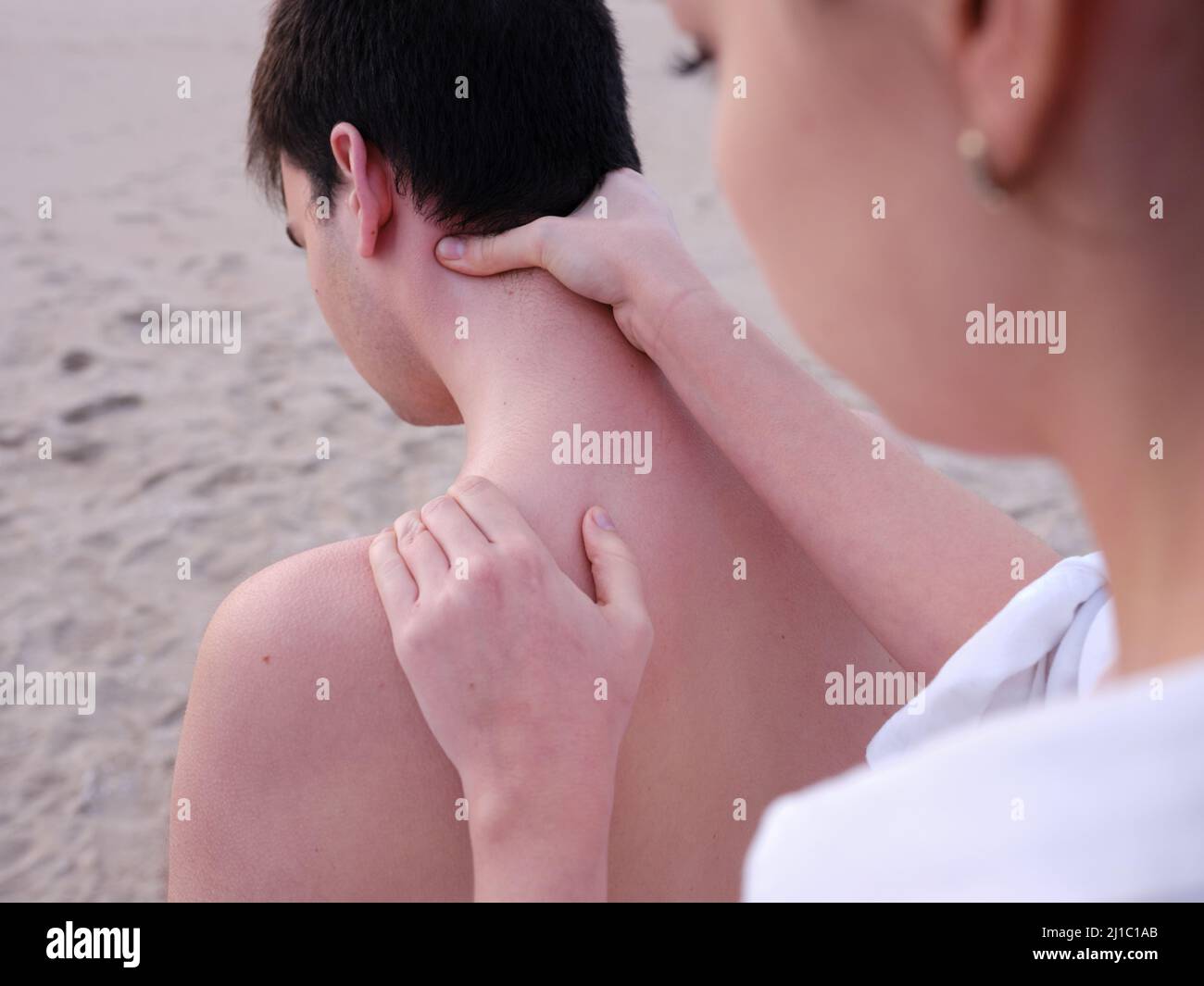 Eine junge Chiromassage-Therapeutin, die einem jungen Mann an einem Strand in Valencia Schulter- und Nackenmassagen gibt. Stockfoto