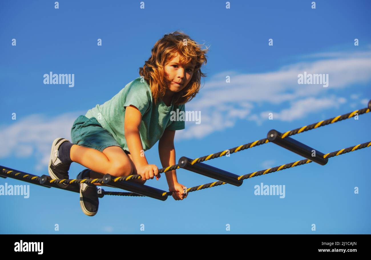 Kind klettert im Netz. Netter Junge klettert die Leiter auf dem Spielplatz hoch. Kind klettert die Leiter gegen den blauen Himmel hinauf. Stockfoto