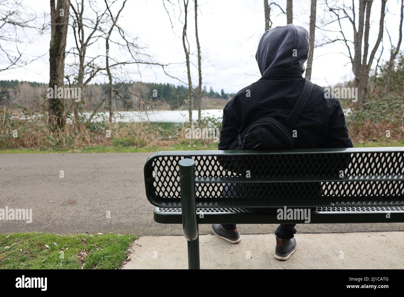 Person, die auf einer grünen Bank am Zementweg vor dem See sitzt. Stockfoto