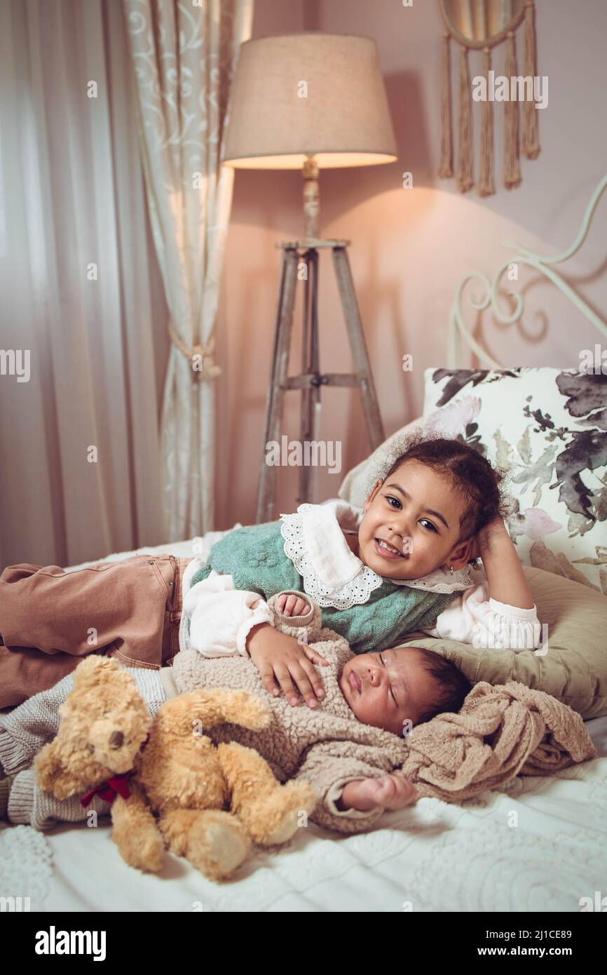 Kleines multiethnisches Mädchen, Schwester, die neben ihrem schlafenden kleinen Bruder auf dem Bett liegt Stockfoto