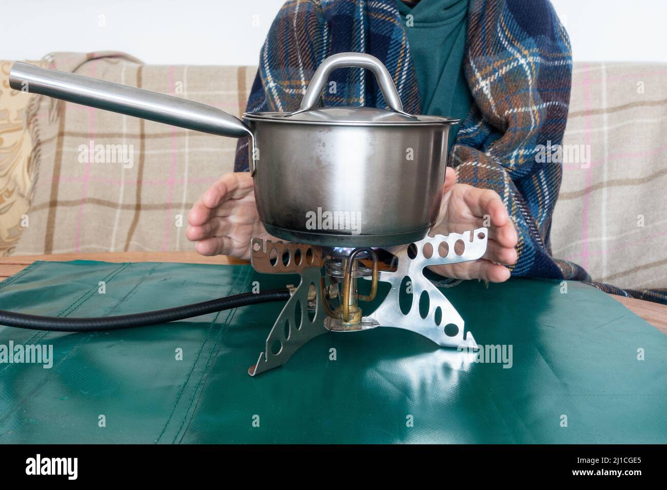 Person, die sich die Hände erwärmt, während er das Essen auf dem Campinggasherd im Haus erwärmt. Konzept: Lebenshaltungskosten, steigende, Gas-, Energie-, Strompreise, Armut Stockfoto