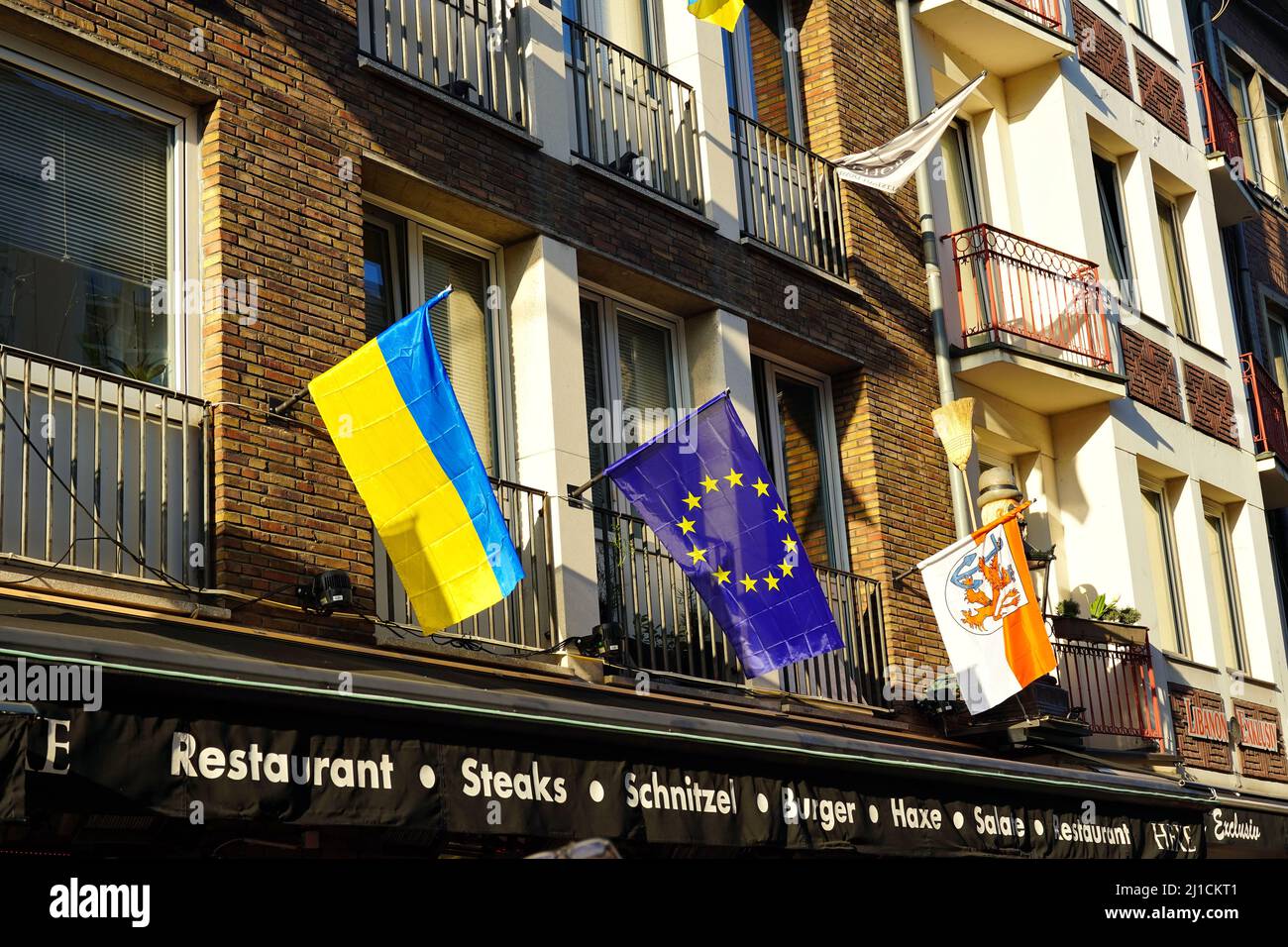 Nahaufnahme verschiedener lokaler und internationaler Flaggen (Ukraine-Flagge, EU-Flagge, Düsseldorf-Flagge) vor einem Restaurant in der Düsseldorfer Altstadt. Stockfoto