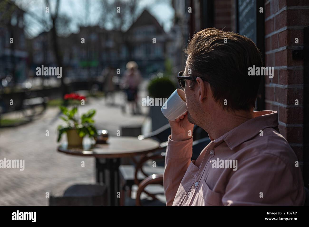 Weißer, unkenntlich kaukasischer Mann in legerer Kleidung hält im Frühling eine Tasse Kaffee und trinkt ihn auf der Terrasse. Stockfoto