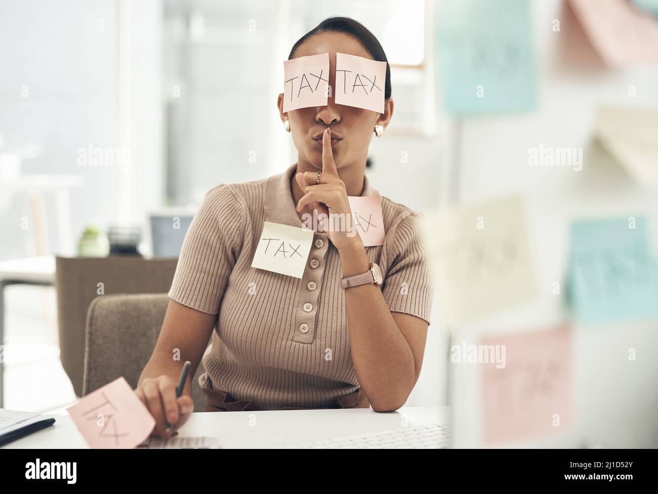 Steuerhinterziehung ist ein Verbrechen. Aufnahme einer jungen Geschäftsfrau, die mit Haftnotizen bedeckt war und ihre Finger auf den Lippen hielt, während sie in einem Büro an Steuern arbeitete. Stockfoto