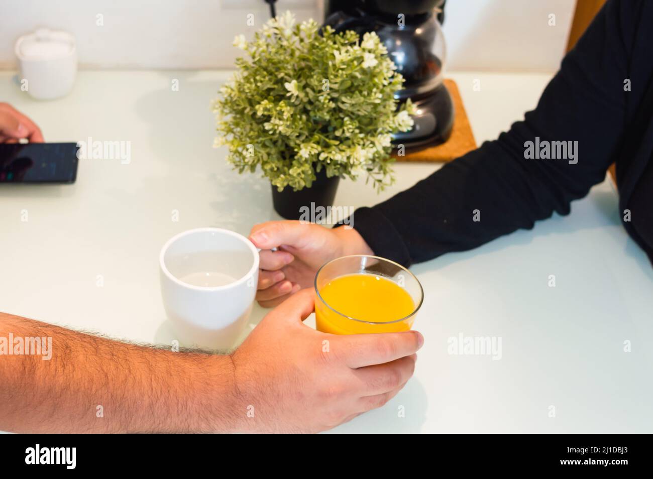 Ehemann und Ehefrau halten Tassen mit Saft nebeneinander auf der Theke, kaukasisches Paar in der Küche zu Hause in einem liebevollen Moment zusammen im bre Stockfoto