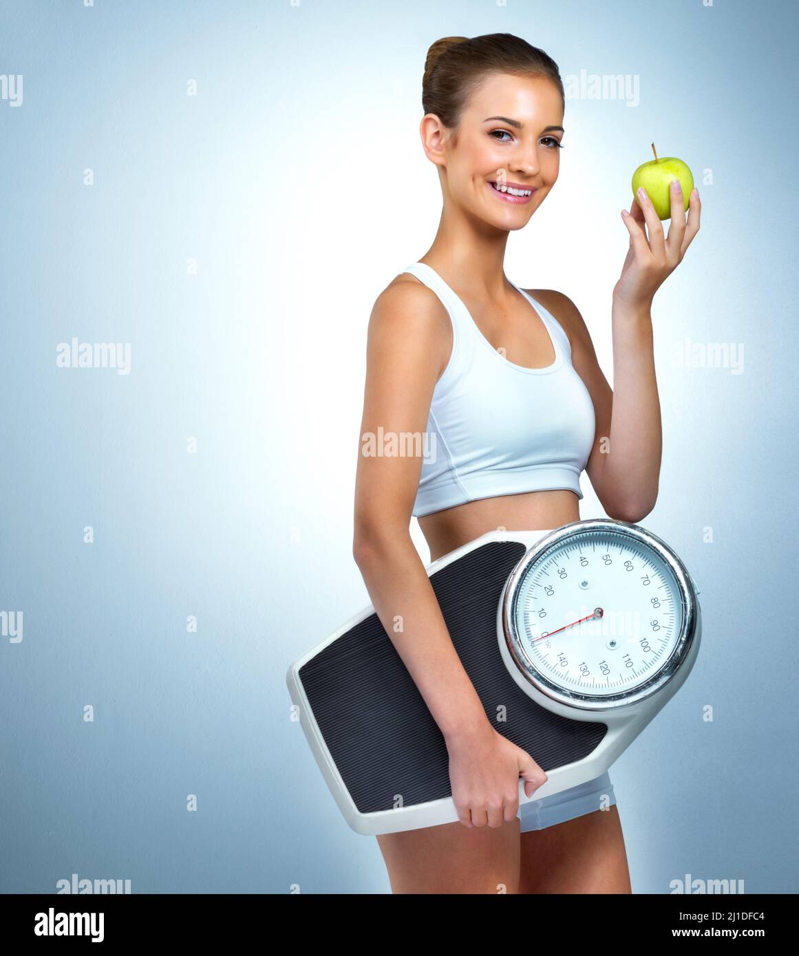 Weniger eine Diät, mehr ein Lebensstil. Porträt einer gesundheitsbewussten jungen Frau, die mit einem Apfel und einer Waage im Studio posiert. Stockfoto