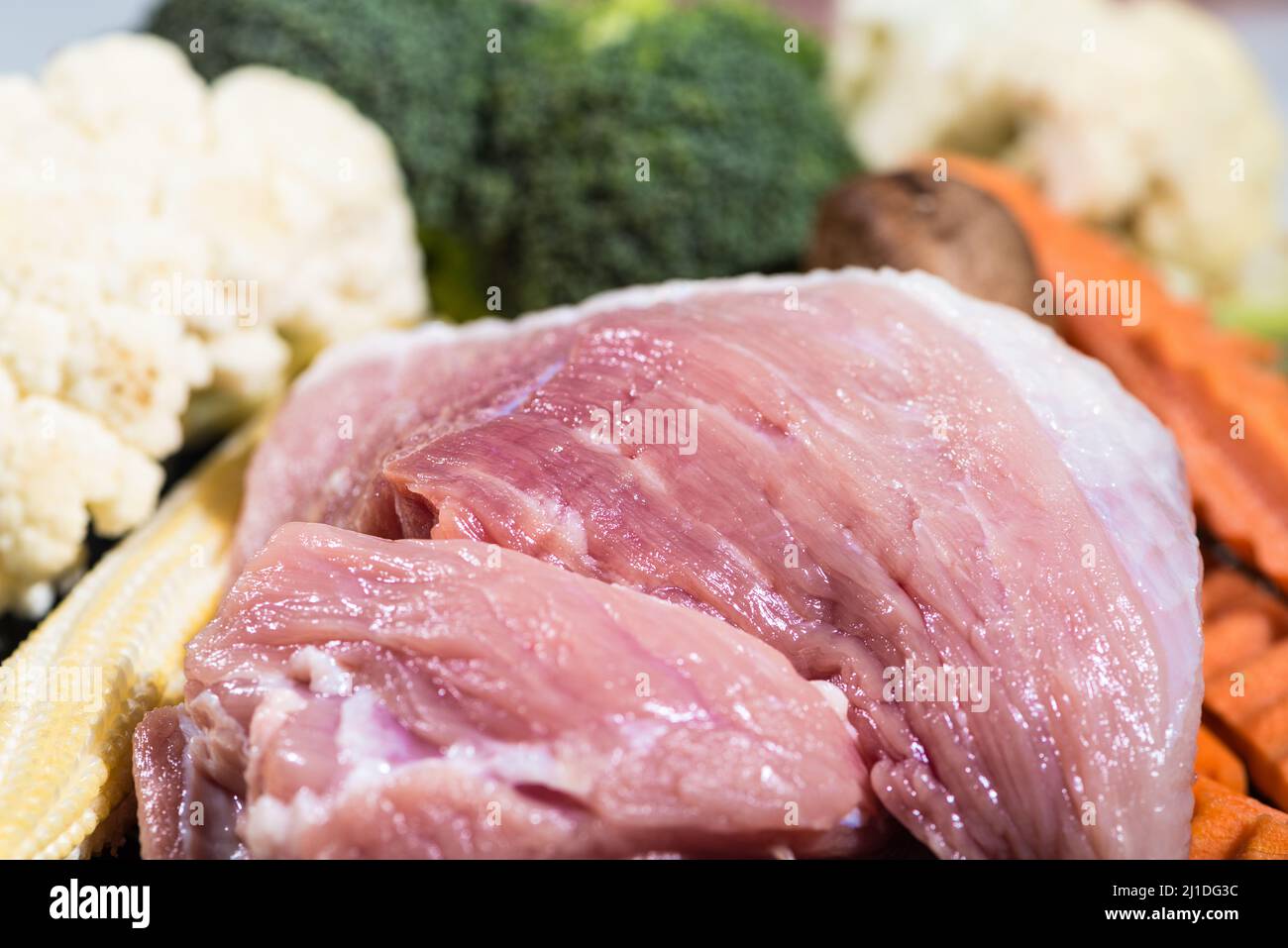 Close up piece frisches rohes Schweinefleisch und viele Gemüsesorten sind Babykorn, Brokkoliblüten, Pilze, Karotten, Blumenkohl Zutaten für die Zubereitung von Lebensmitteln Stockfoto