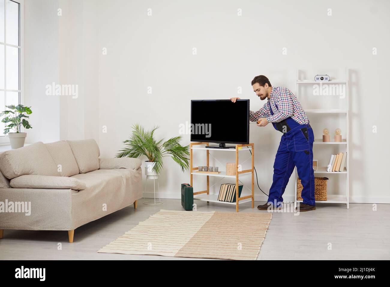 Junger professioneller männlicher Fernsehtechniker installiert und verbindet neuen Fernseher im Haus des Kunden. Stockfoto