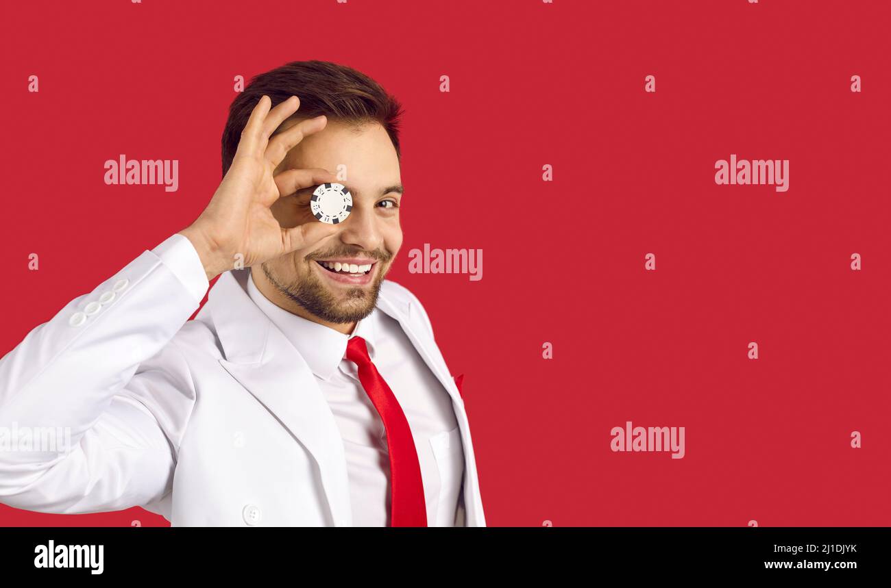 Glücklicher junger Mann auf rotem Kopierraum Hintergrund hält Poker-Chip auf seinem Auge Stockfoto
