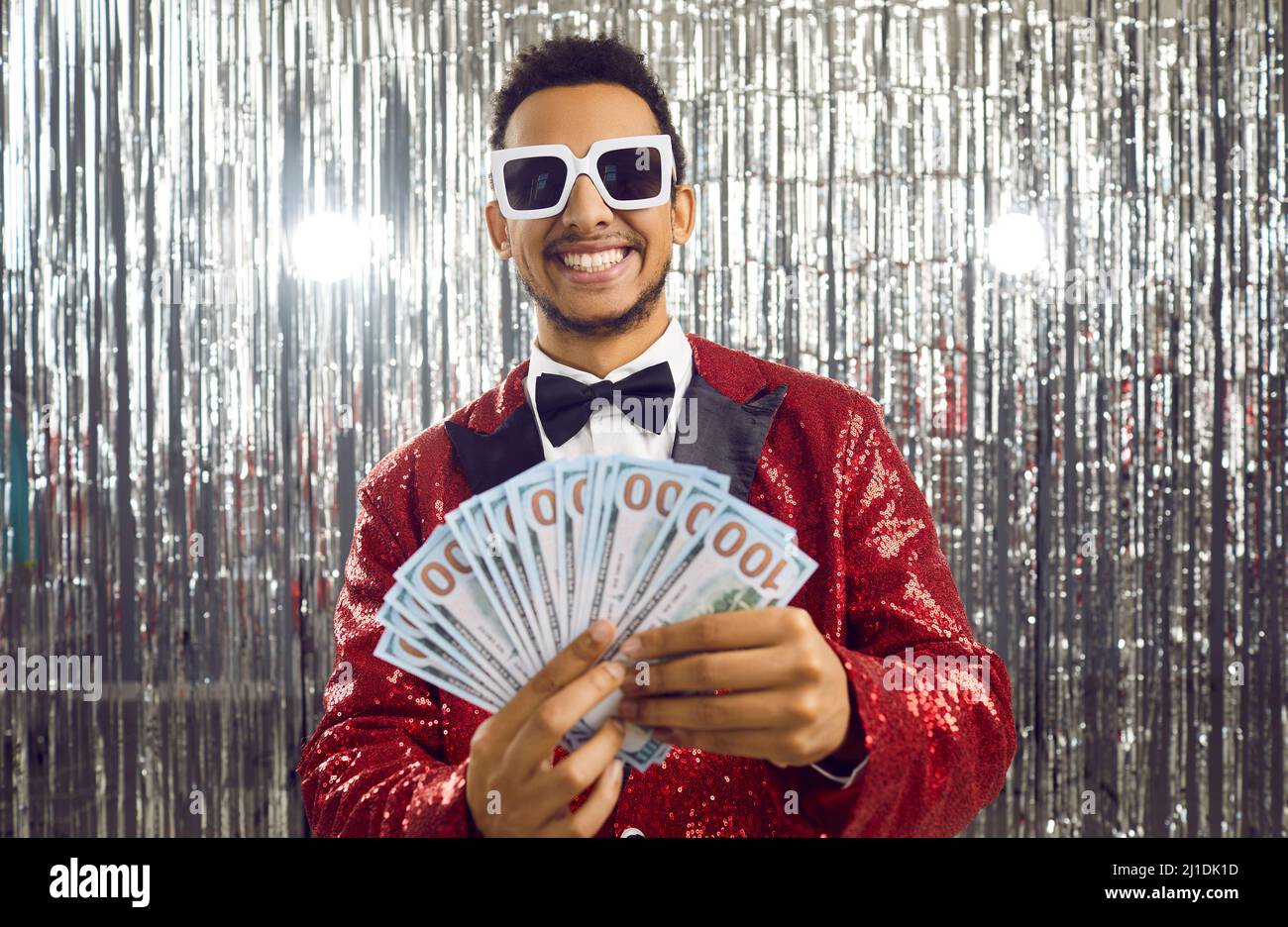 Glücklicher schwarzer Kerl, der viel Geld gewonnen hat, indem er einen Haufen Banknoten hält und lächelt Stockfoto