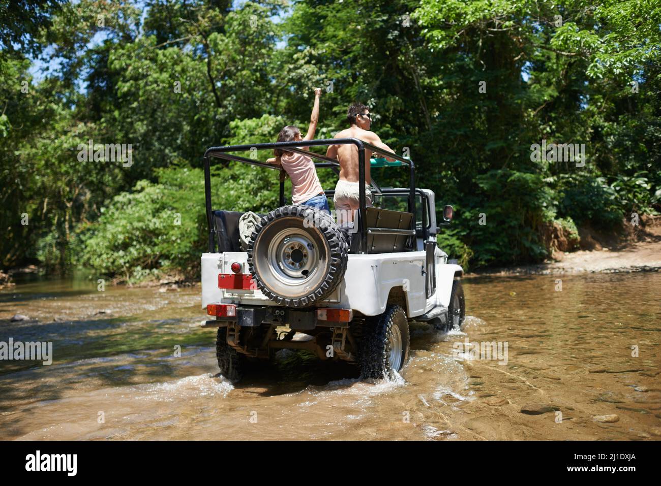 Auf ihrer Reise in extremes Gelände. Aufnahme eines jungen Paares, das in seinem Geländewagen durch einen Fluss fährt. Stockfoto