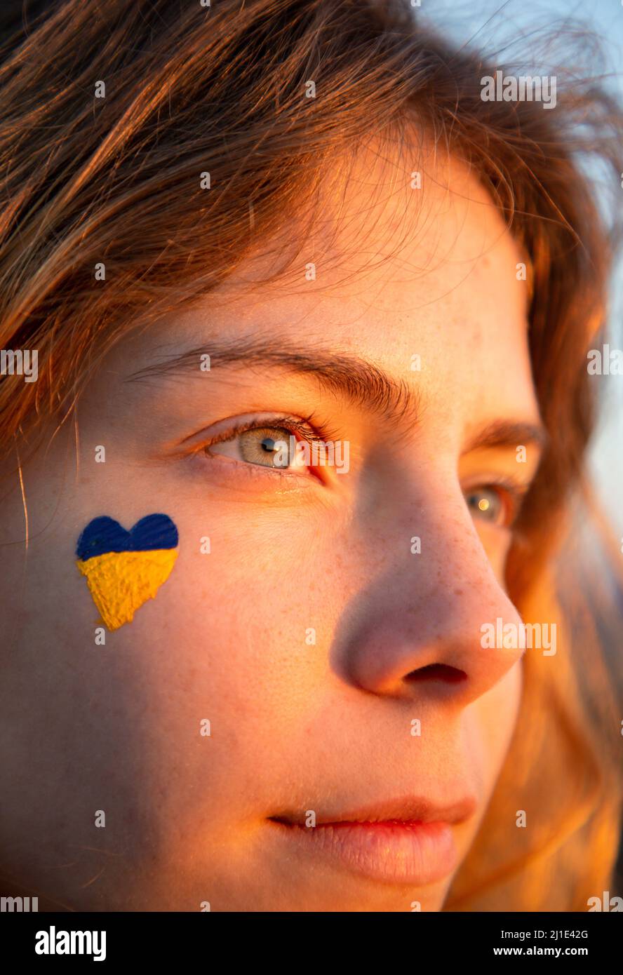 Nahaufnahme eines weiblichen Gesichts mit einem gelb-blauen Herzen auf der Wange. Sonnenlicht Bei Sonnenuntergang. Schau nach vorne. Unterstützt Die Ukraine. Vertrauen in den Sieg Stockfoto