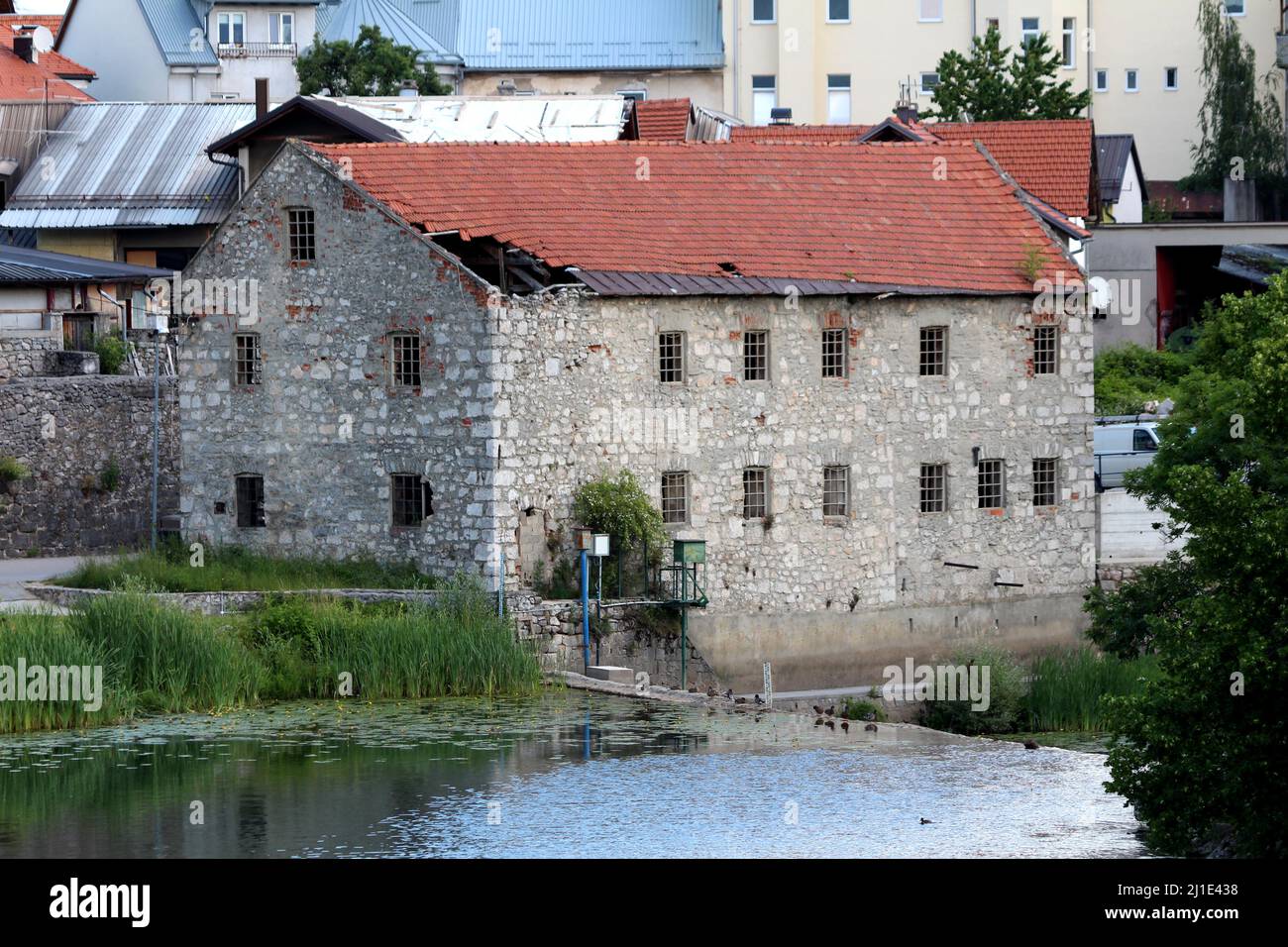 Großes verlassene altes Gebäude mit traditionellen Steinwänden und Betonrahmenfenstern ohne Glas, die mit kaputten roten Dachziegeln bedeckt sind Stockfoto