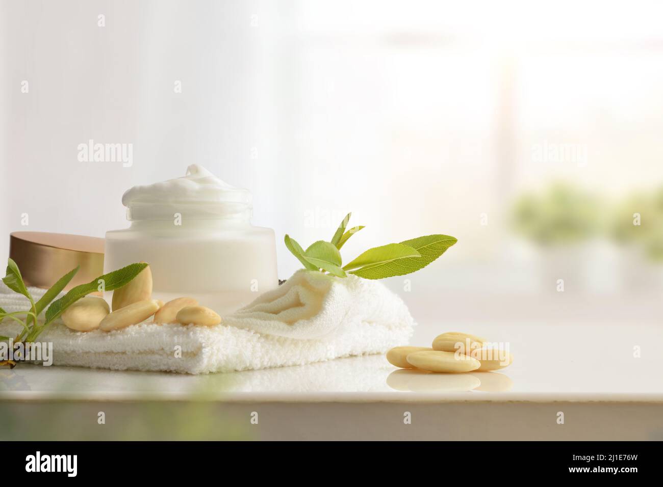 Feuchtigkeitsspendende Creme mit Mandelextrakt auf weißem Tisch mit Früchten im Badezimmer. Vorderansicht. Horizontale Zusammensetzung. Stockfoto
