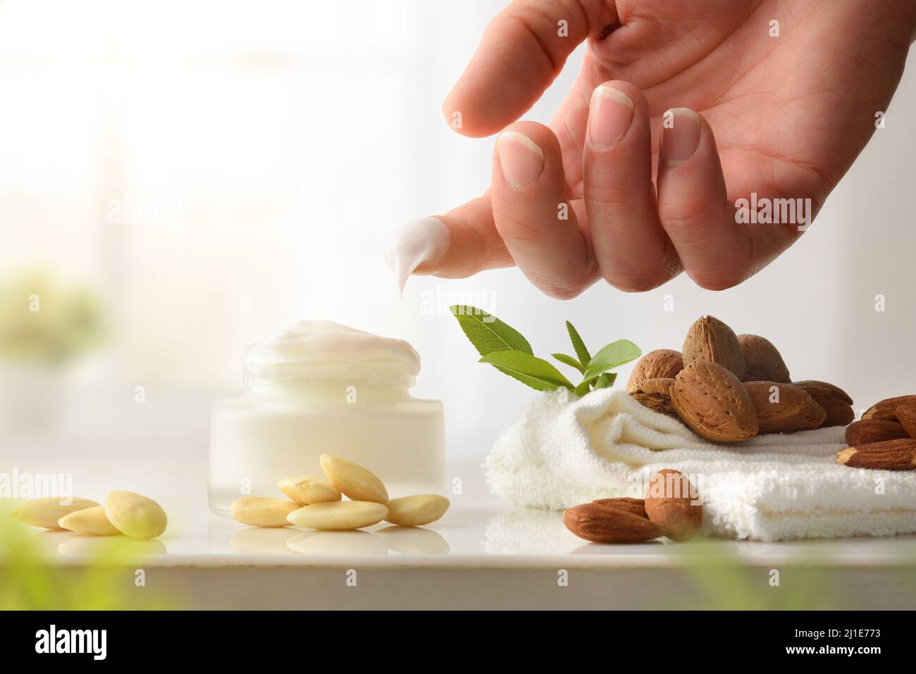 Hand Anwendung feuchtigkeitsspendende Creme mit Extrakt aus Mandeln und Früchten auf dem Tisch im Badezimmer. Vorderansicht. Horizontale Zusammensetzung. Stockfoto
