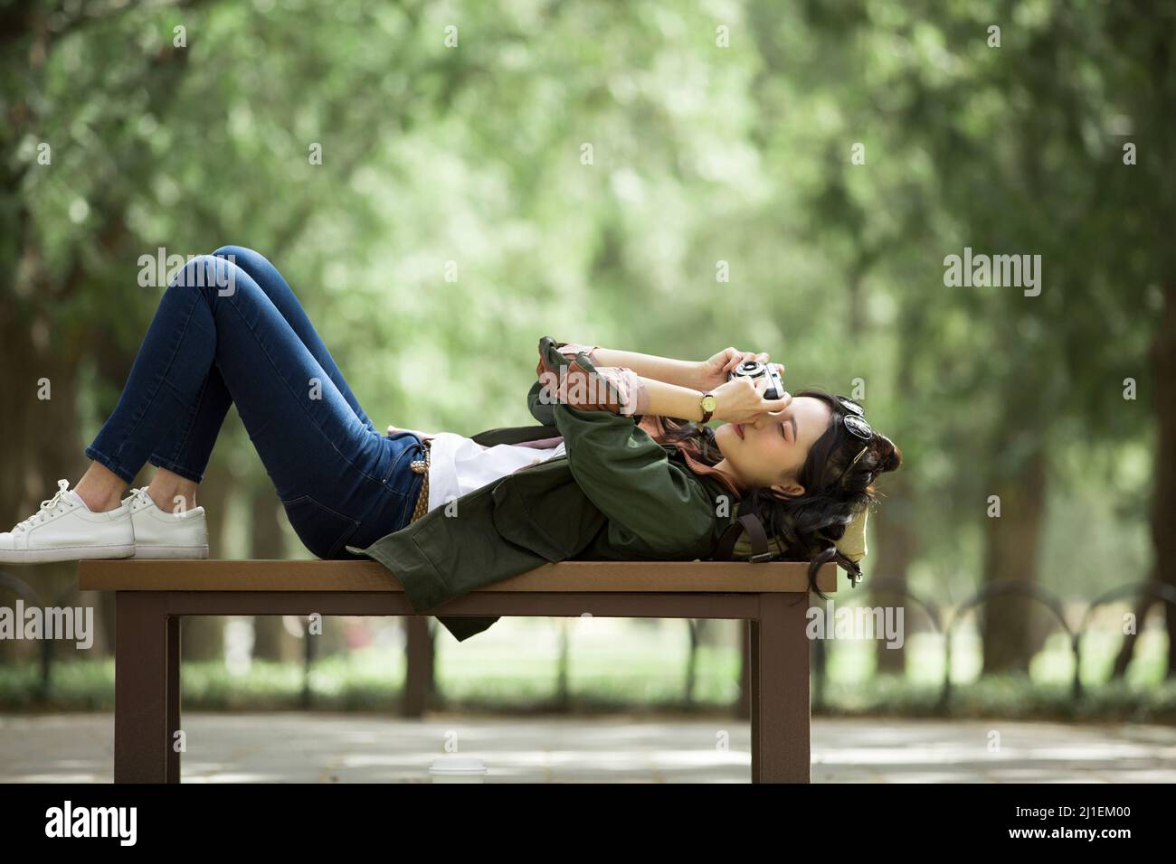 Junge Touristenin auf einer Bank liegend und fotografiert - Stock Photo Stockfoto