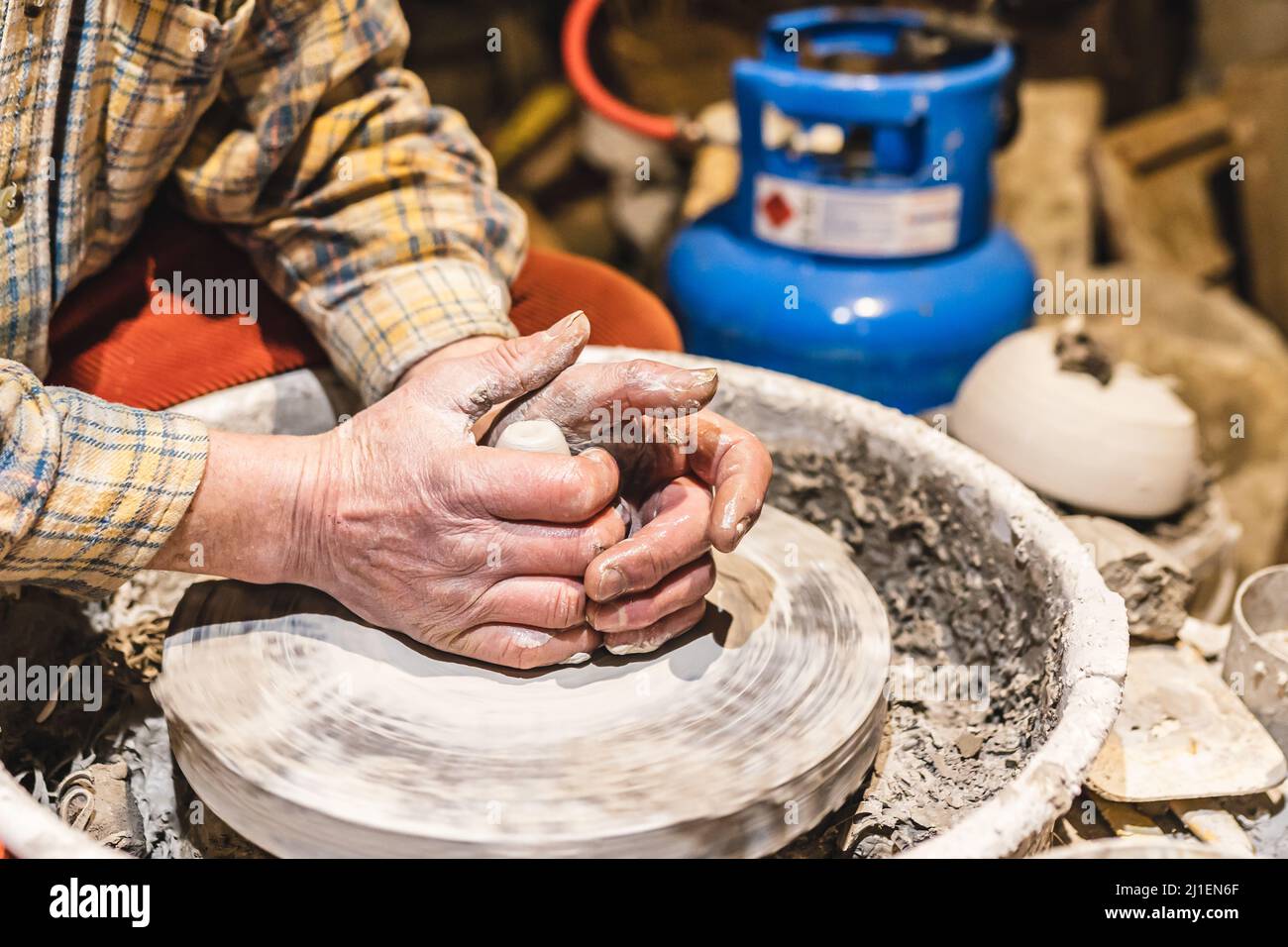 Muskulöse Hände eines Mannes mittleren Alters, Töpfer, in Ton verschmutzt, bilden Tonwaren aus Ton auf dem Töpferrad Stockfoto
