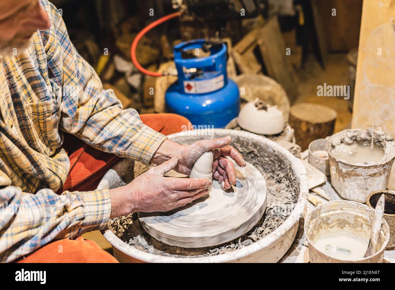 Muskulöse Hände eines Mannes mittleren Alters, Töpfer, in Ton verschmutzt, bilden Tonwaren aus Ton auf dem Töpferrad Stockfoto