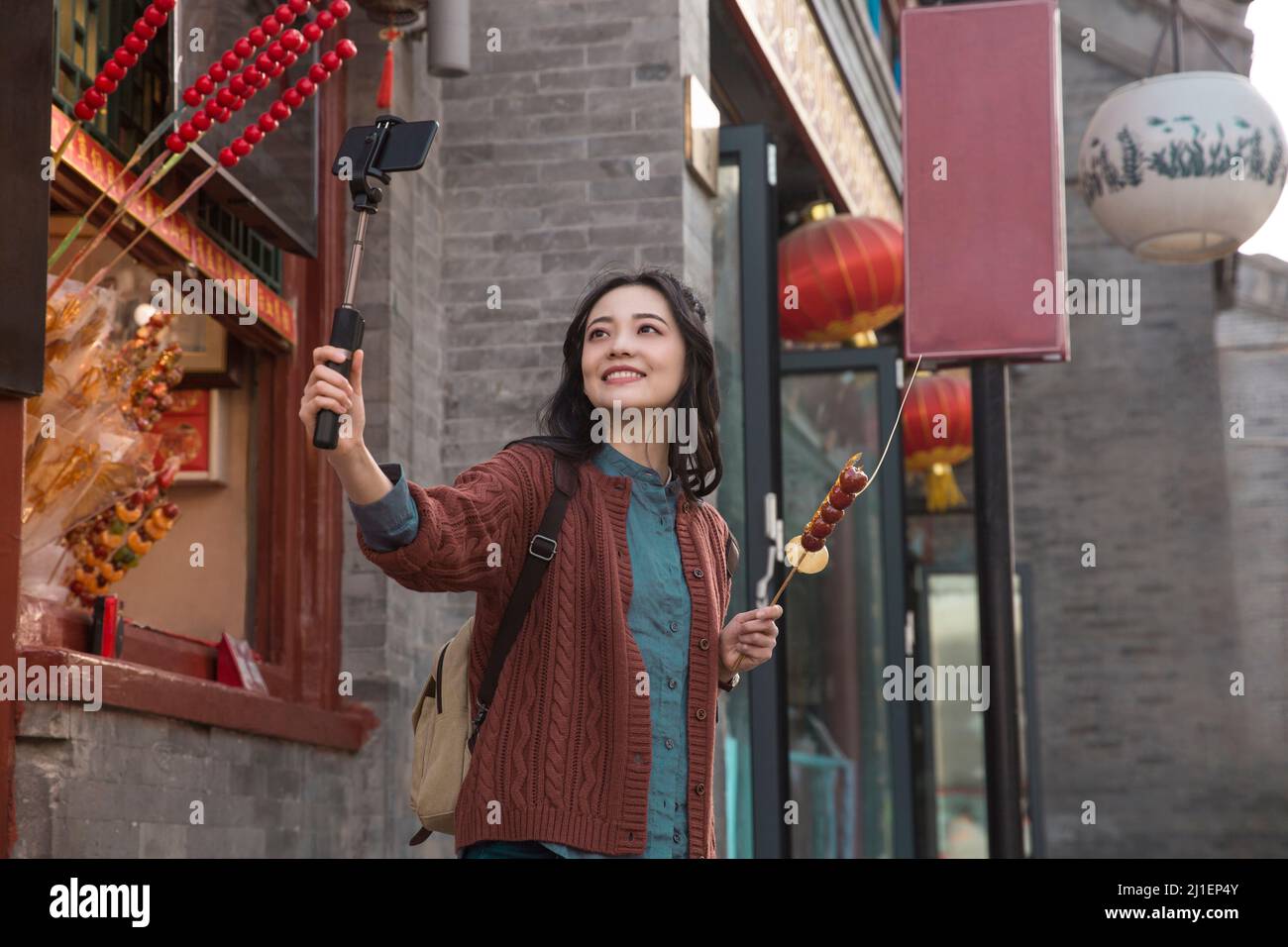 Backpacker-Frau, die Selfie in einem Food-Stand in einer Fußgängerzone im klassischen Stil macht, mit Tanghulu und Tangren - Stockfoto Stockfoto