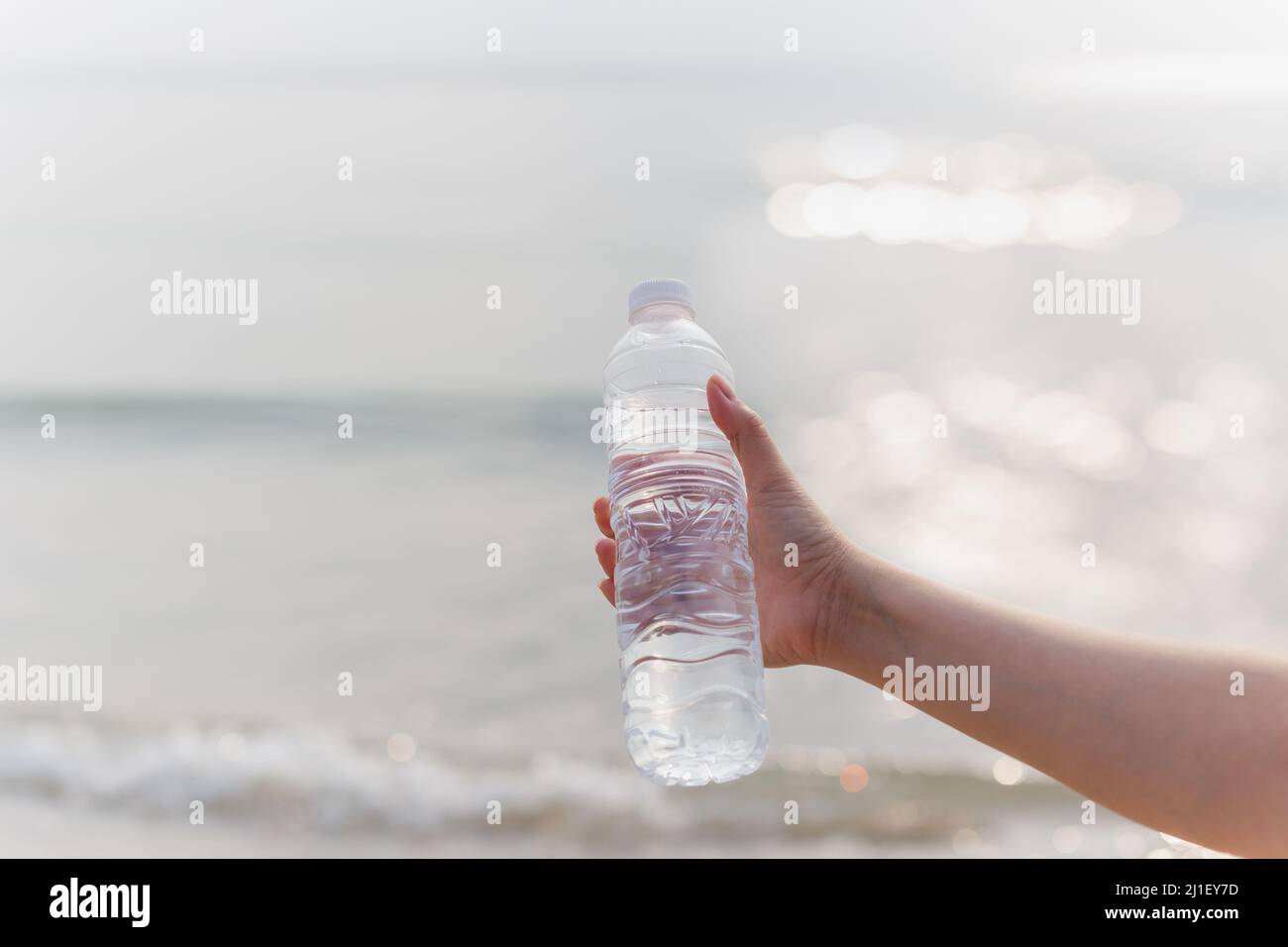 Eine Frau, die am Strand eine Flasche Mineralwasser in der Hand hält. Stockfoto