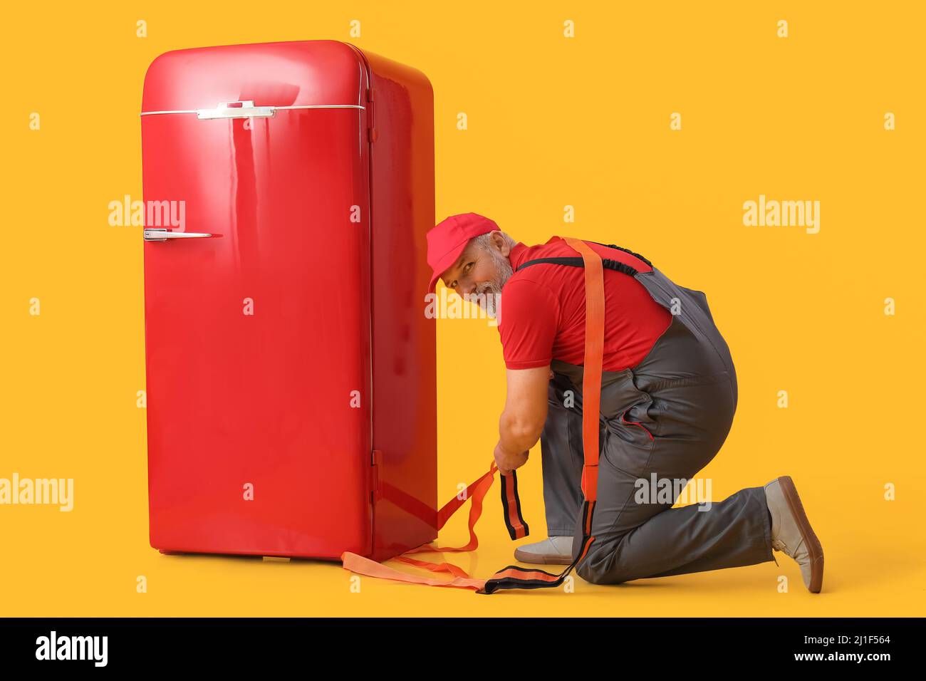 Reifer Arbeiter mit Tragegurt und Retro-Kühlschrank auf gelbem Hintergrund Stockfoto