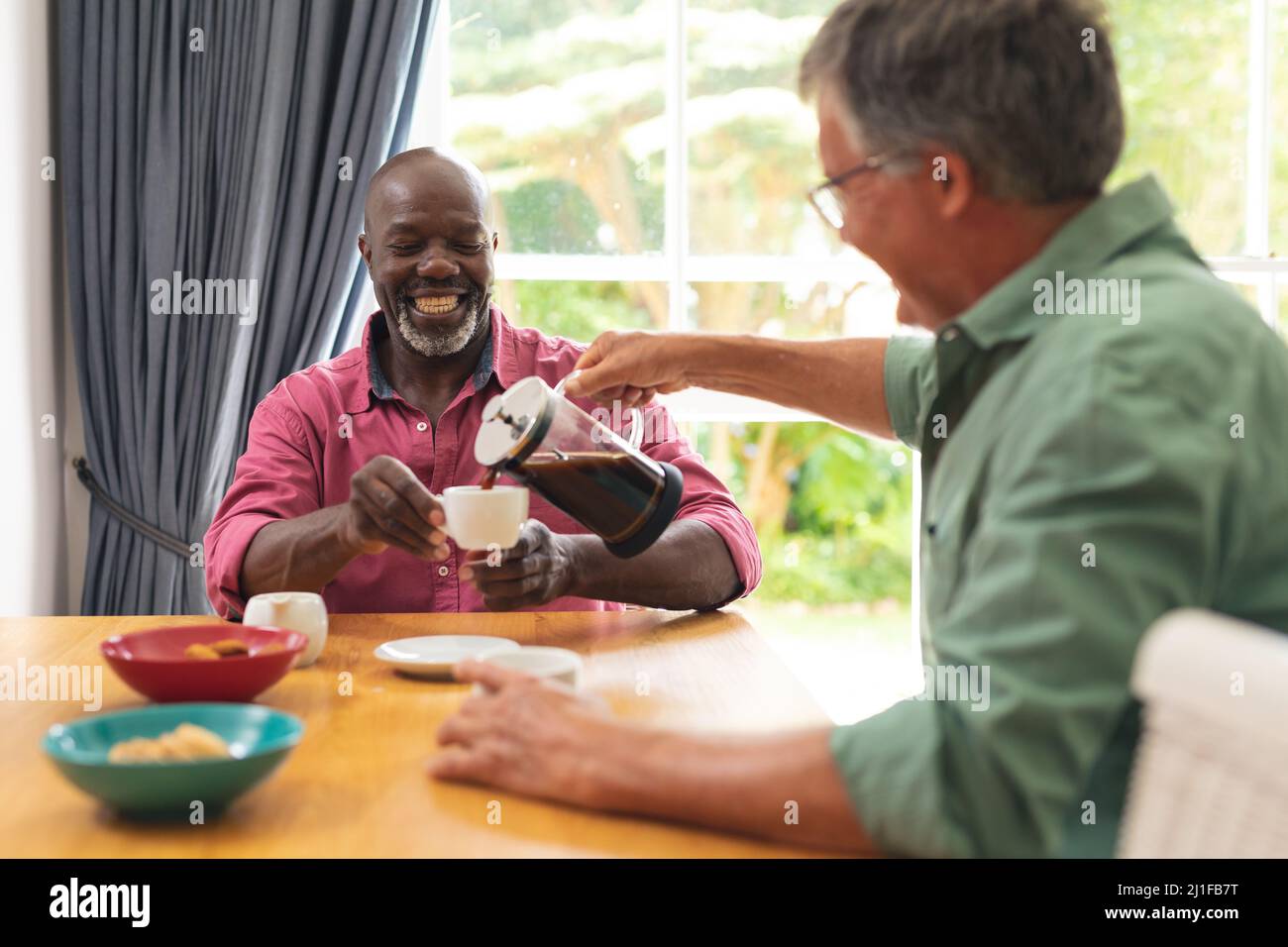 Glückliche kaukasische und afroamerikanische ältere männliche Freunde, die zu Hause Kaffee trinken Stockfoto