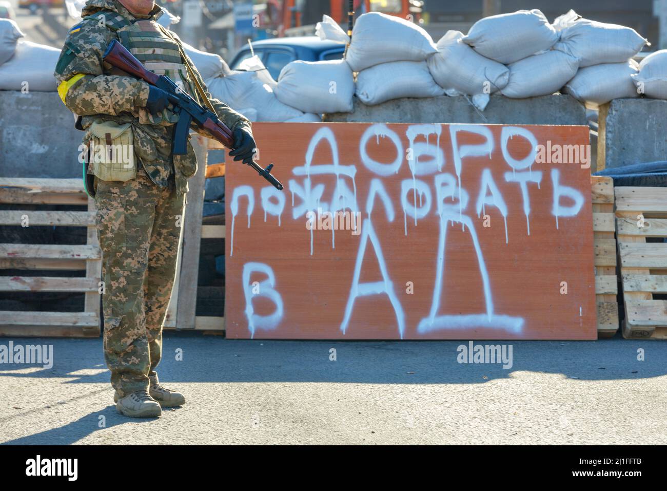 Willkommen zur Hölleninschrift auf einem Holzschild am Checkpoint Kiew, wo der Verteidiger der territorialen Verteidigung an einem sonnigen Frühlingstag zeigt. Stockfoto